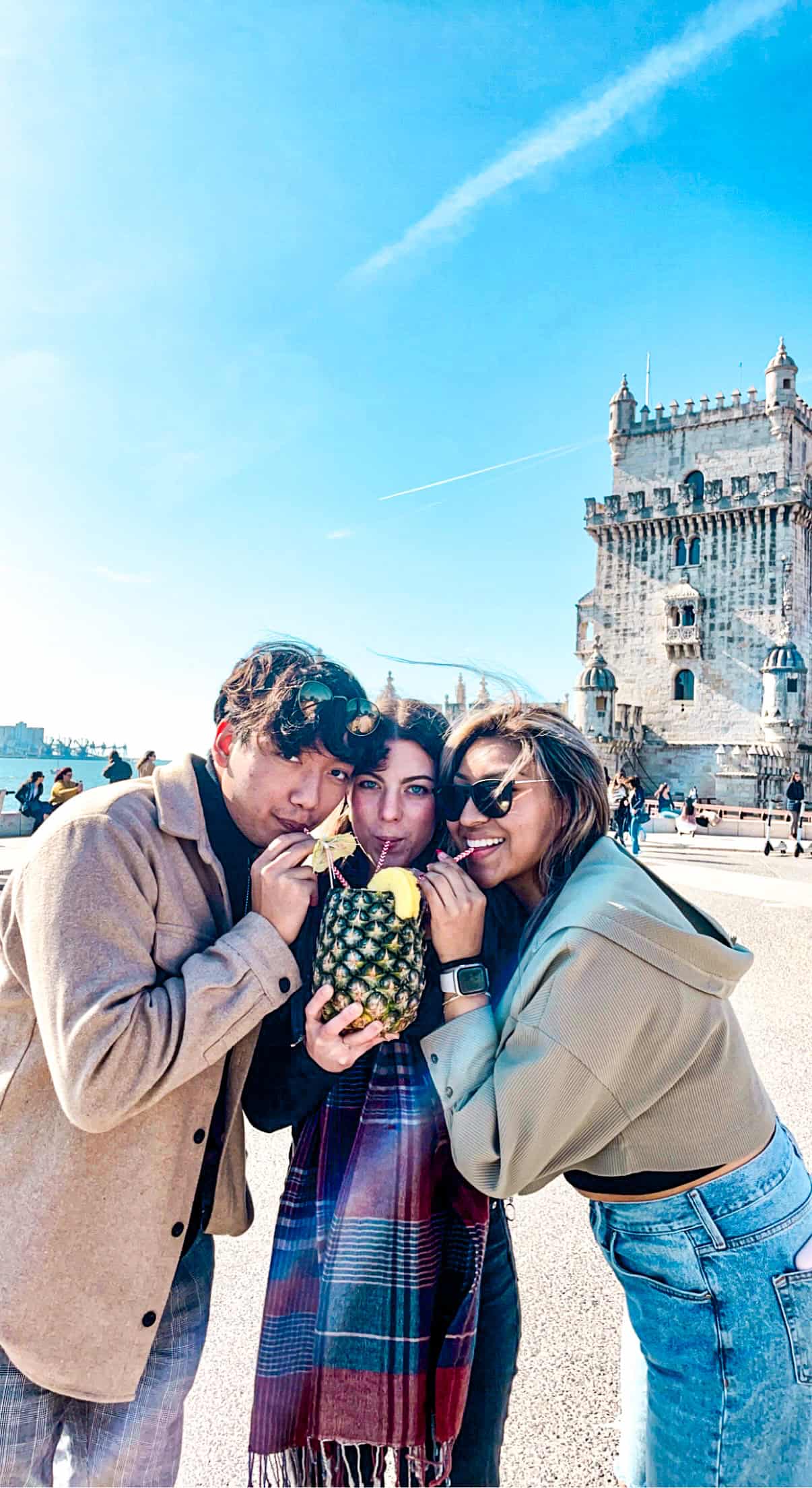 Three people sharing a drink out of a pineapple at the Belem Tower in Lisbon, Portugal