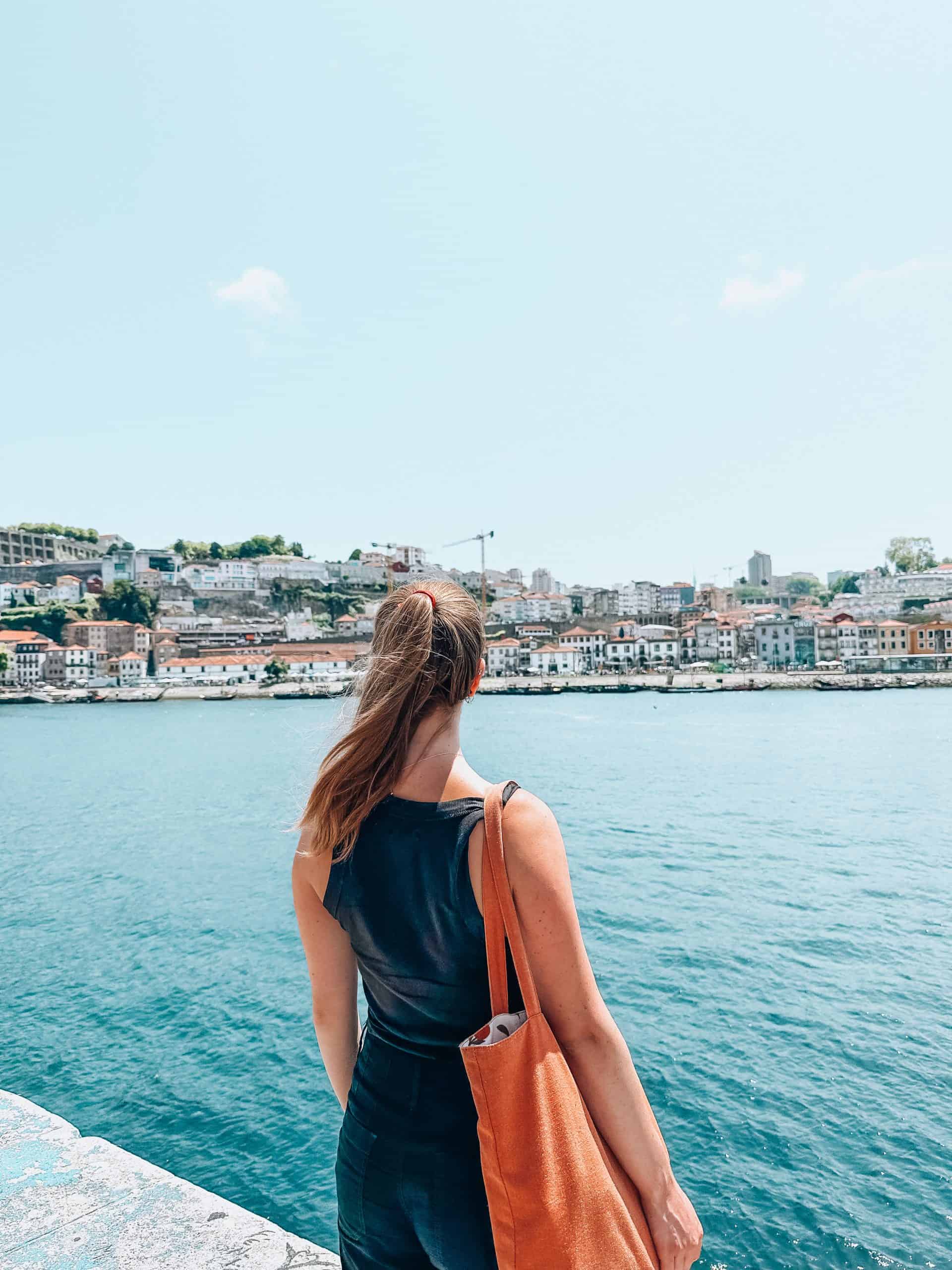 White woman with brunette hair facing towards the Duoro River on a summer day in Porto, Portugal