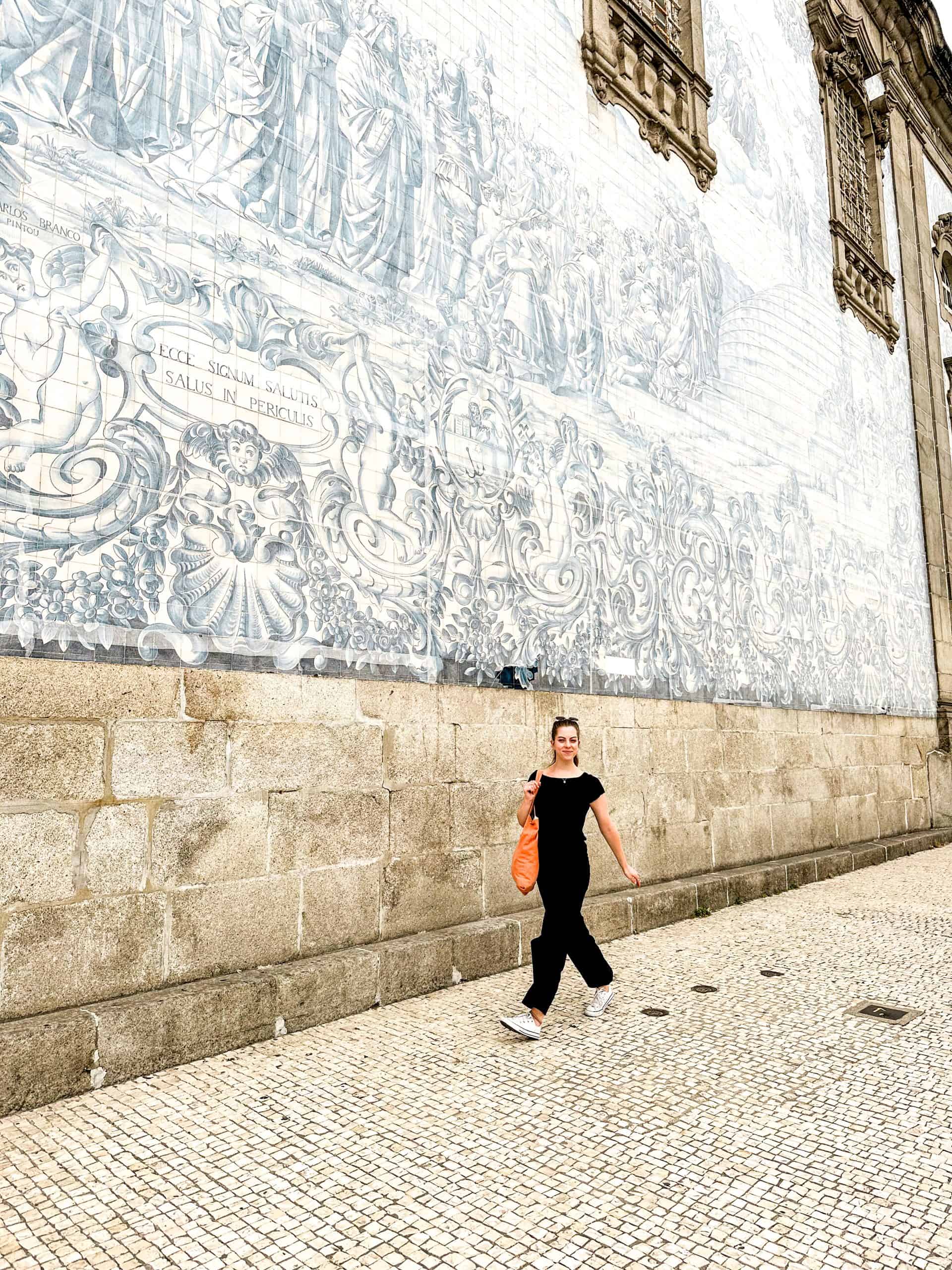 A white woman walking down the street in Porto, Portugal against a blue and white tile background