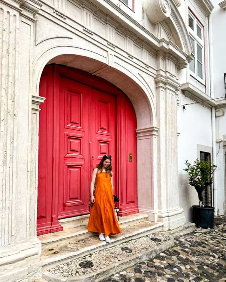 5 Days in Lisbon Woman in a bright orange dress in front of a large pink door in Lisbon, Portugal