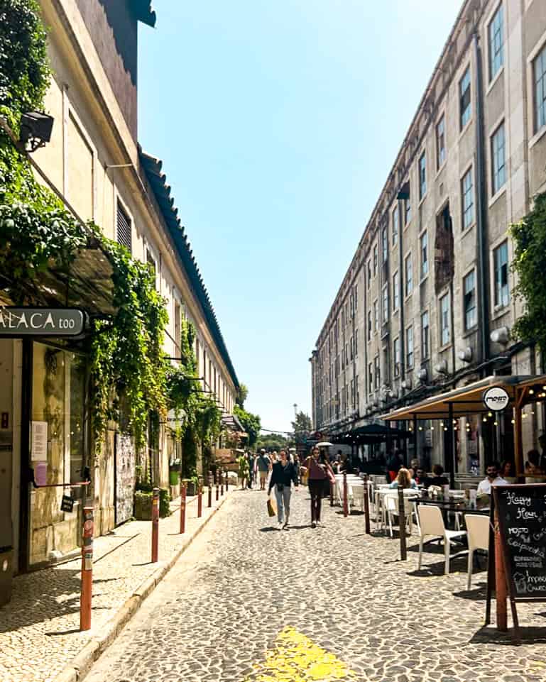 5 Days in Lisbon A cobblestone street with outdoor restaurants on a summer day in Lisbon, Portugal