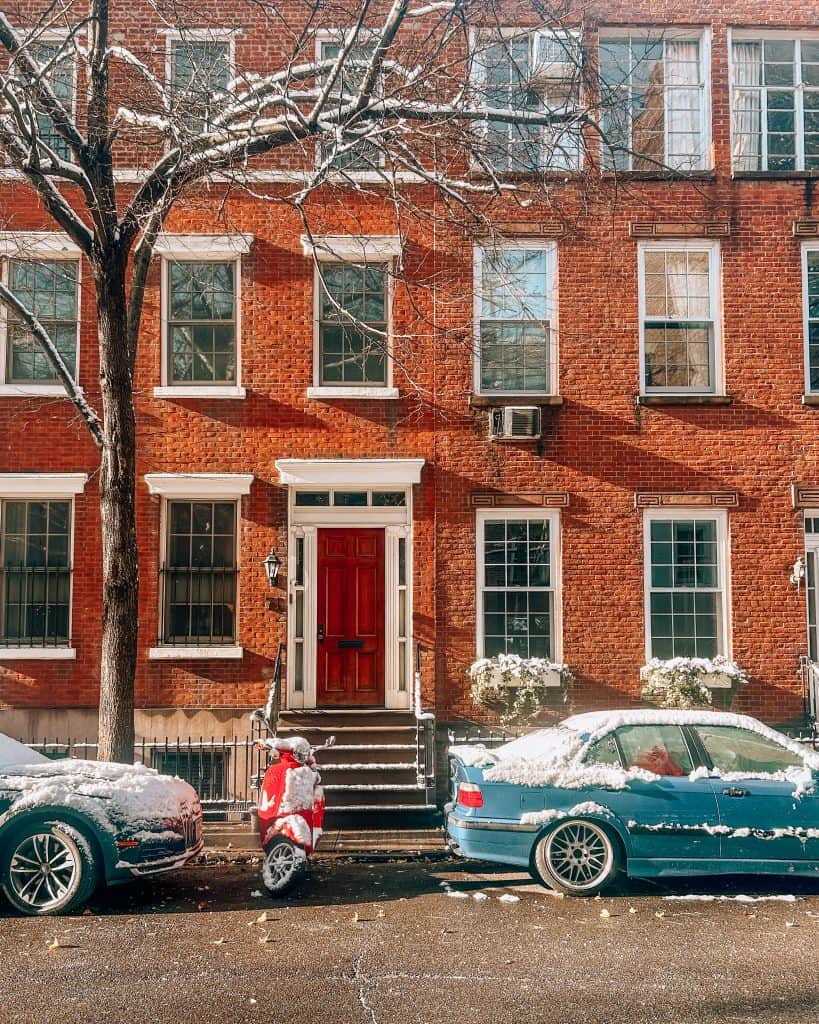 A brick brownstone building with cars and a scooter in front on a West Village street in New York