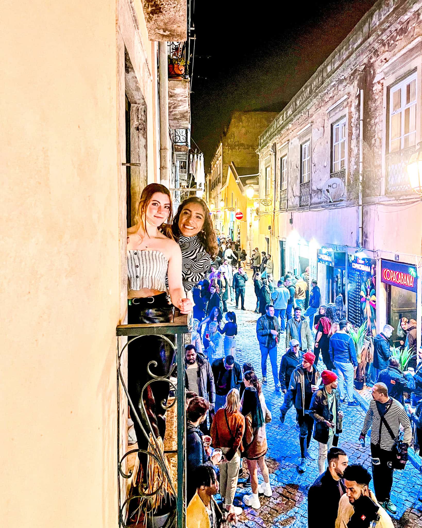 5 Days in Lisbon Two women standing on a balcony above a crowded nightlife area in Lisbon, Portugal