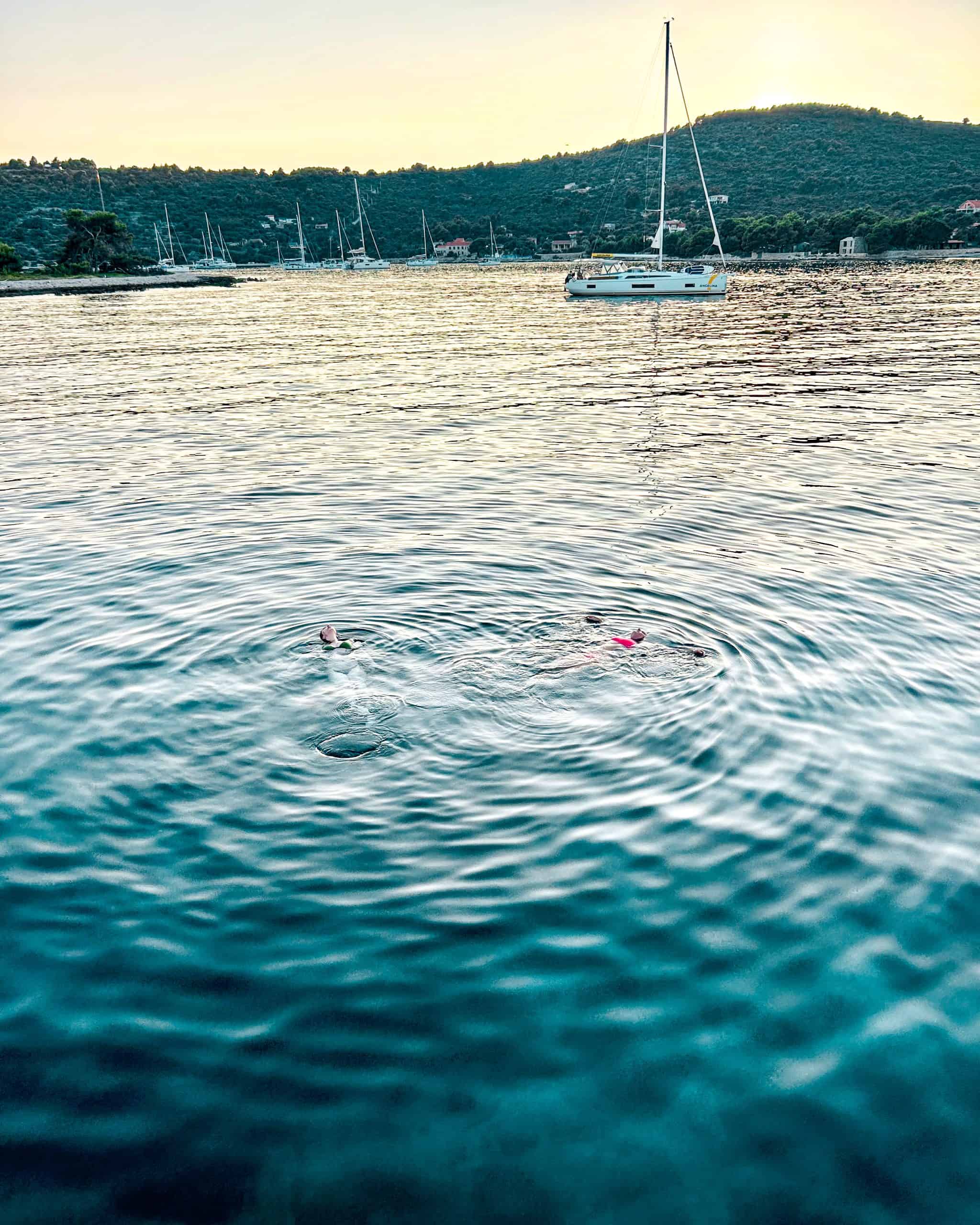 Is Croatia worth visiting? two women floating in the sea with boats in hills in the background in Croatia