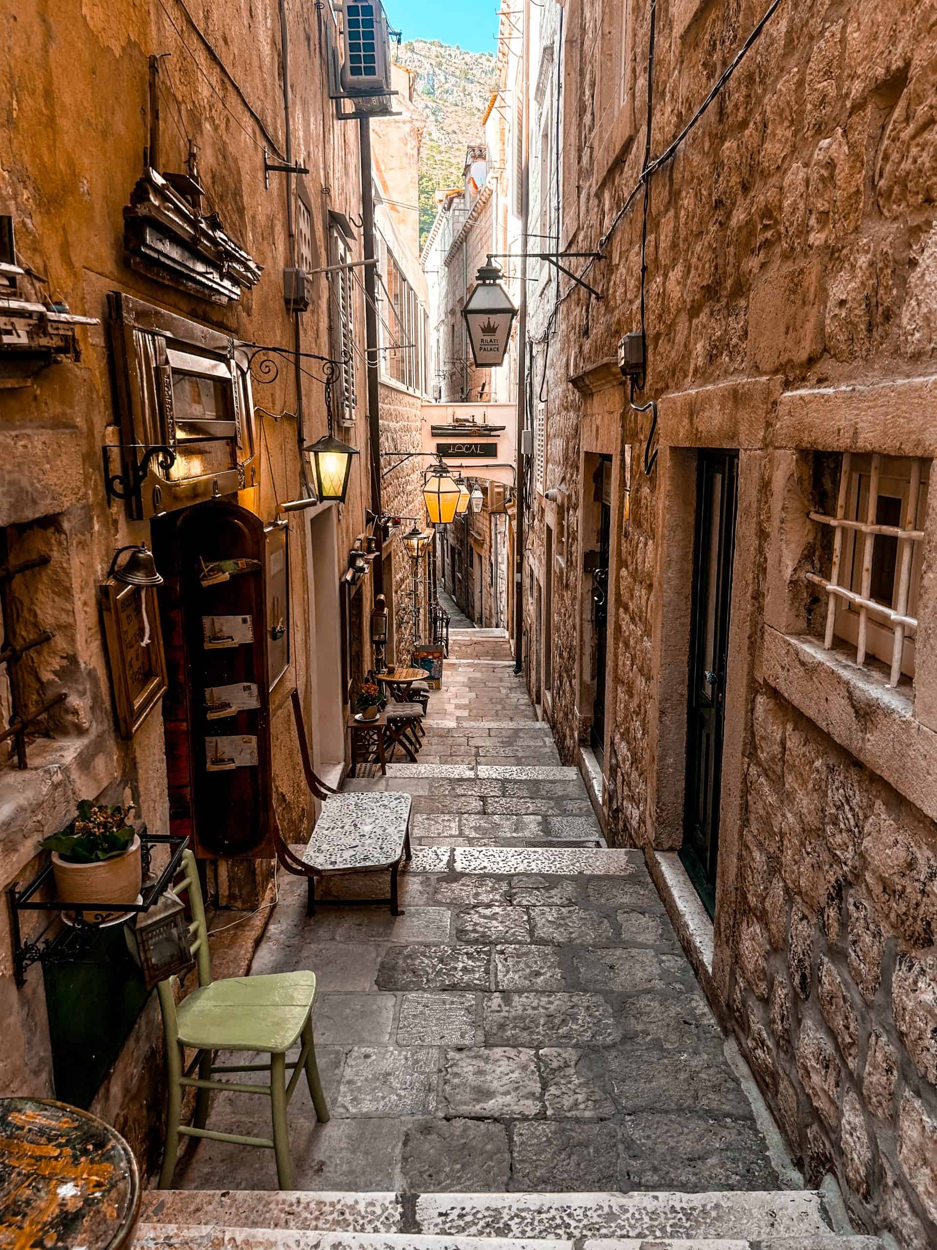 9 days in Croatia Narrow cobble-stone street with chairs and tables and lamps lining the stone buildings on the side in Dubrovnik, Croatia