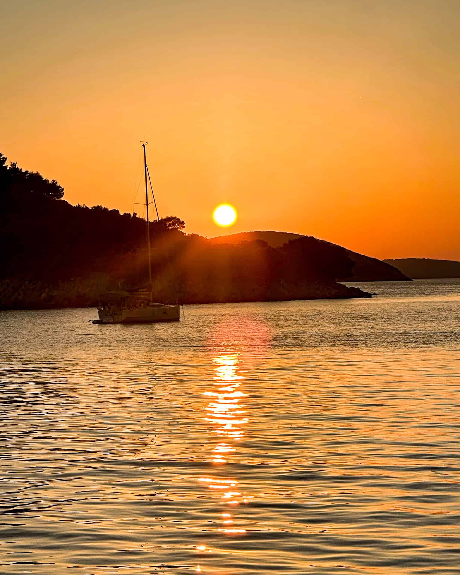 Is Croatia worth visiting? Sunset over the hills on an island in Croatia with a boat and the sea in the foreground