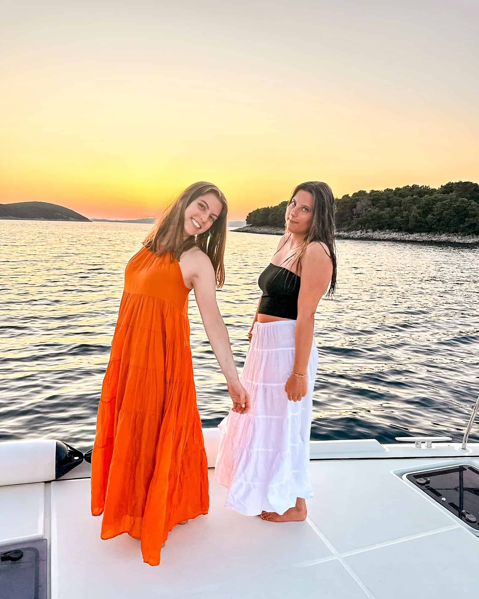9 days in Croatia two young women in an orange dress and black top and white skirt against the sunset on a boat in Croatia