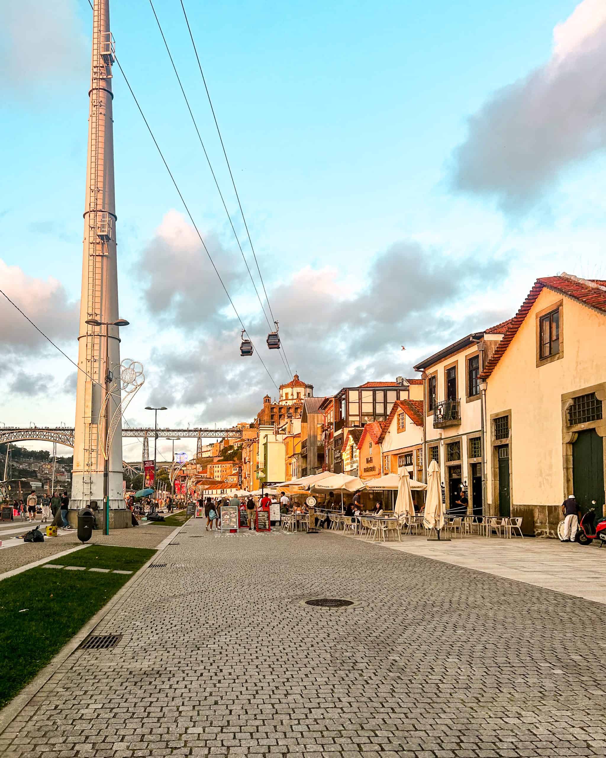 Cobblestone street with restaurants and the gondola overhead at sunset in Porto, Portugal