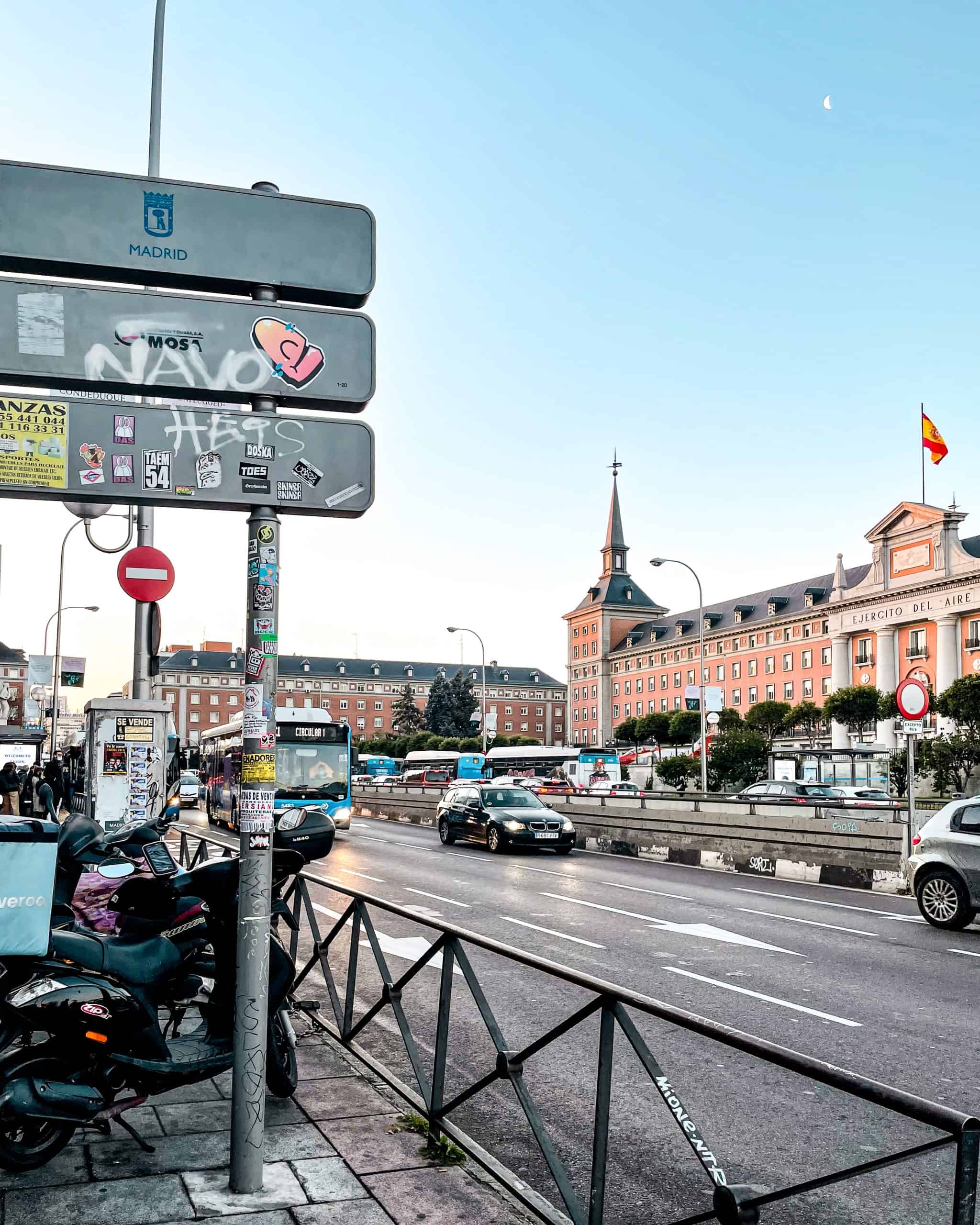 Street in Madrid, Spain with cars, scooters, and busses, and a historic building in the background