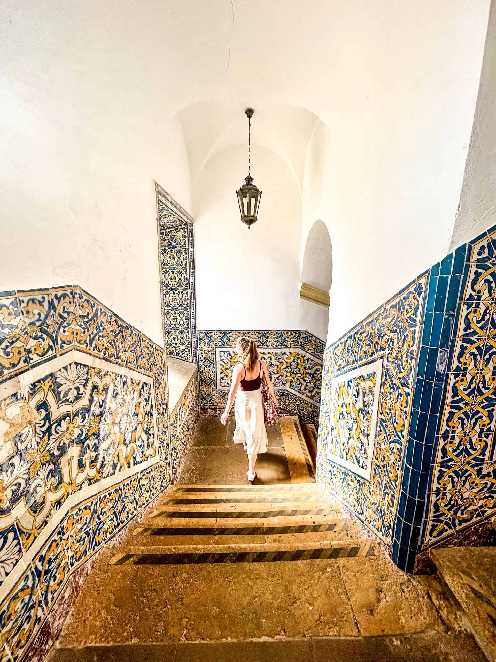 woman waling down the stairs surrounded by blue and yellow tiles in a building in Faro, Portugal