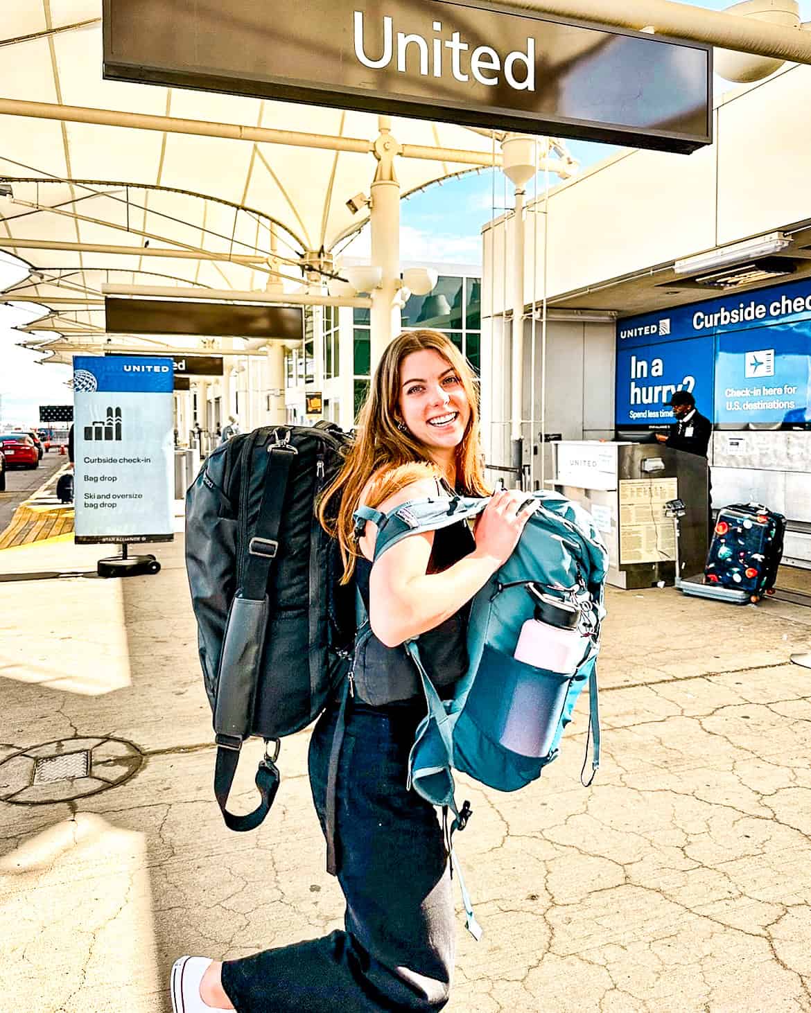 woman with two backpacks standing outside at the airport by the United Airlines sign