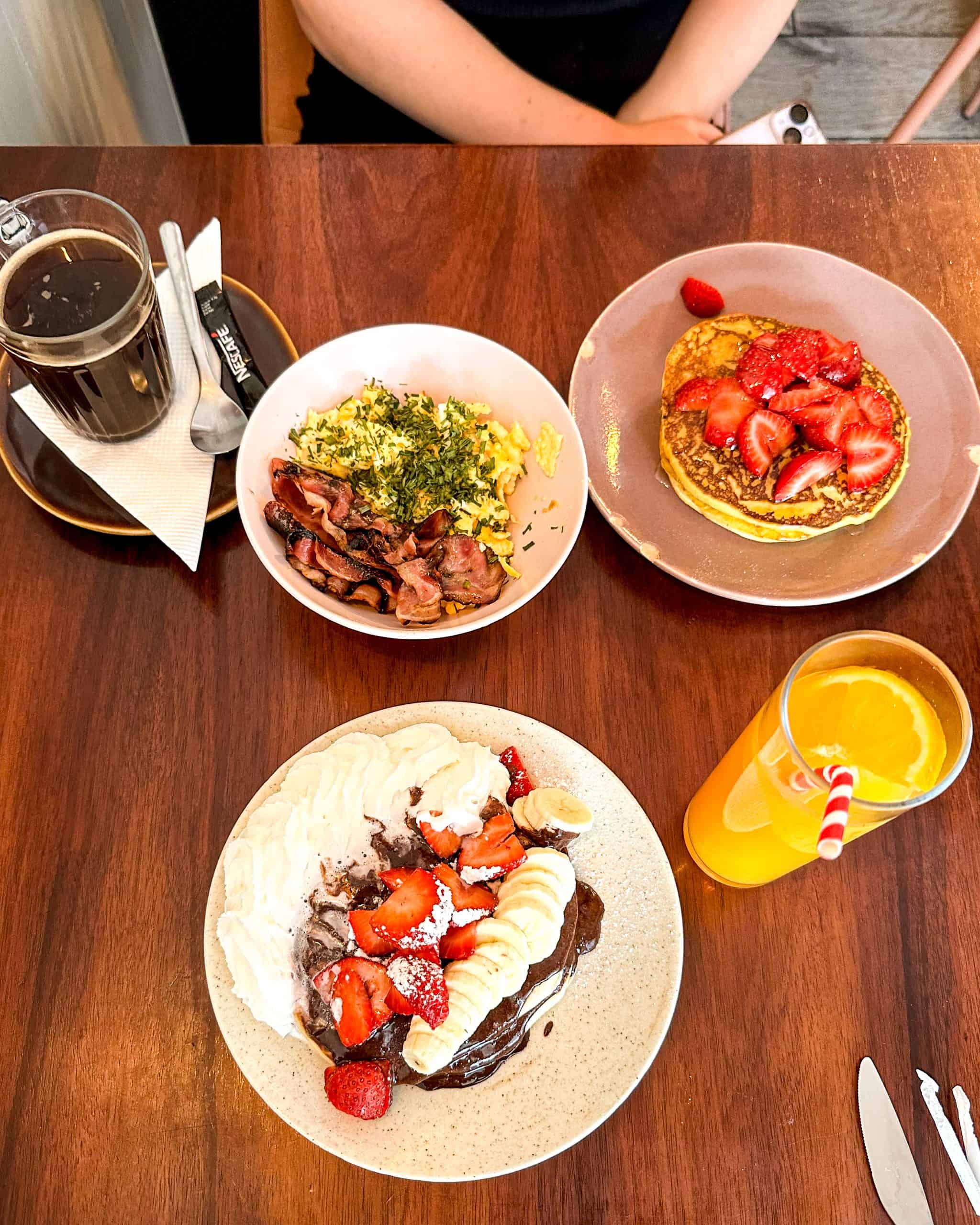 Where to Stay in Porto brunch at a restaurant in Porto, Portugal featuring pancakes with fruit and whipped cream, eggs, bacon, and orange juice