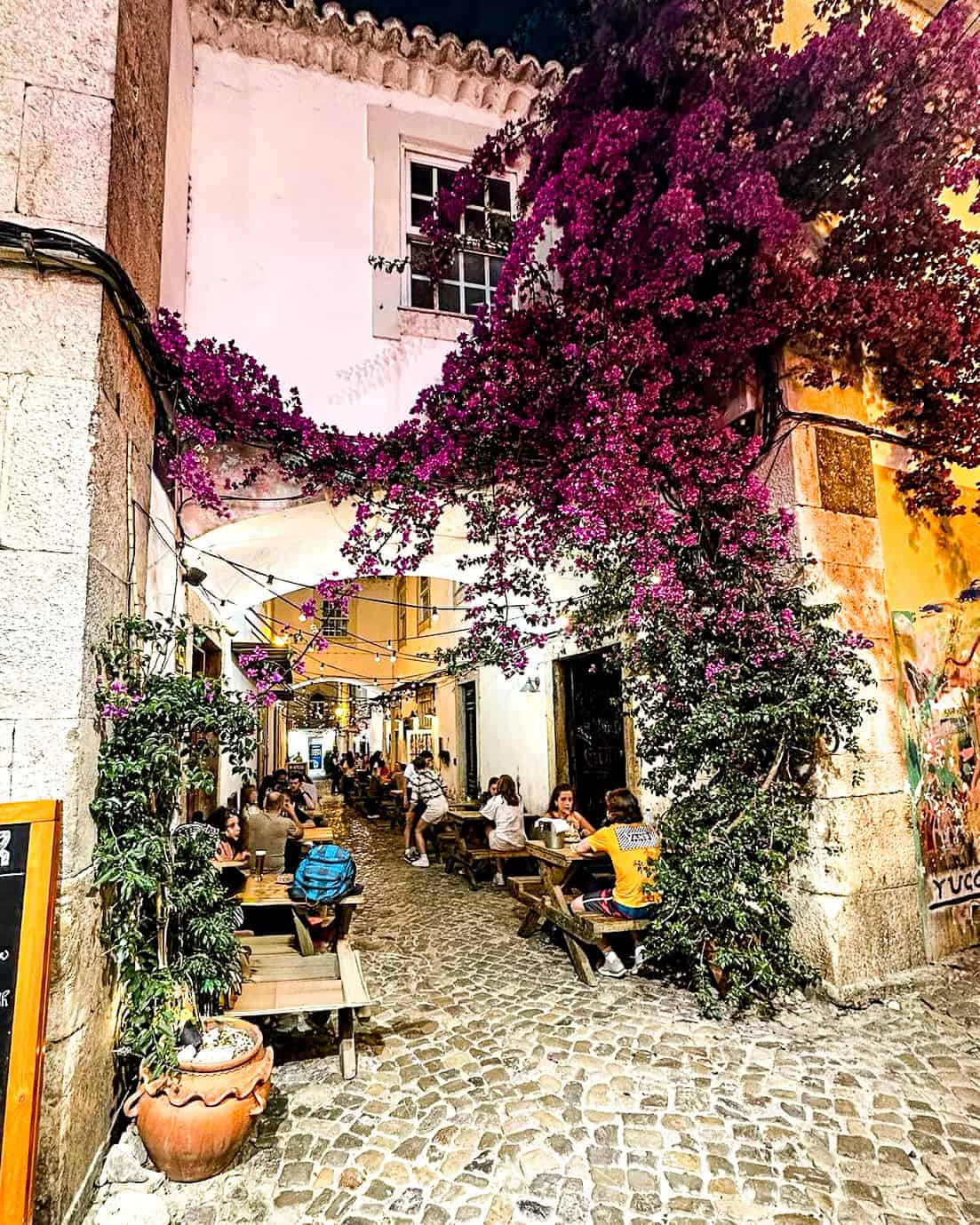 outdoor restaurant on a narrow cobblestone street with hanging vines and flowers above in Faro, Portugal