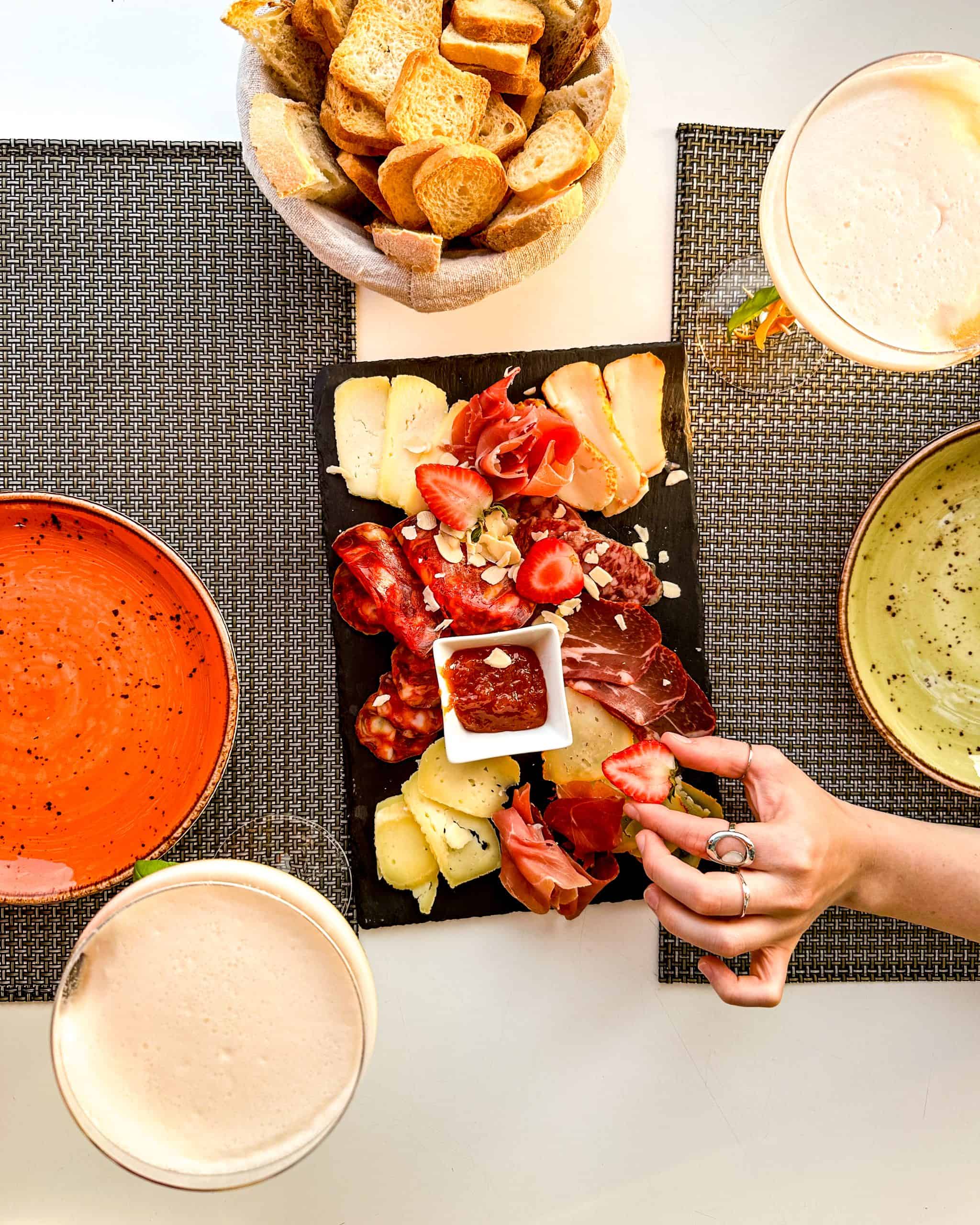 charcuterie board with meats, cheeses, bread and strawberries with colorful plates and drinks