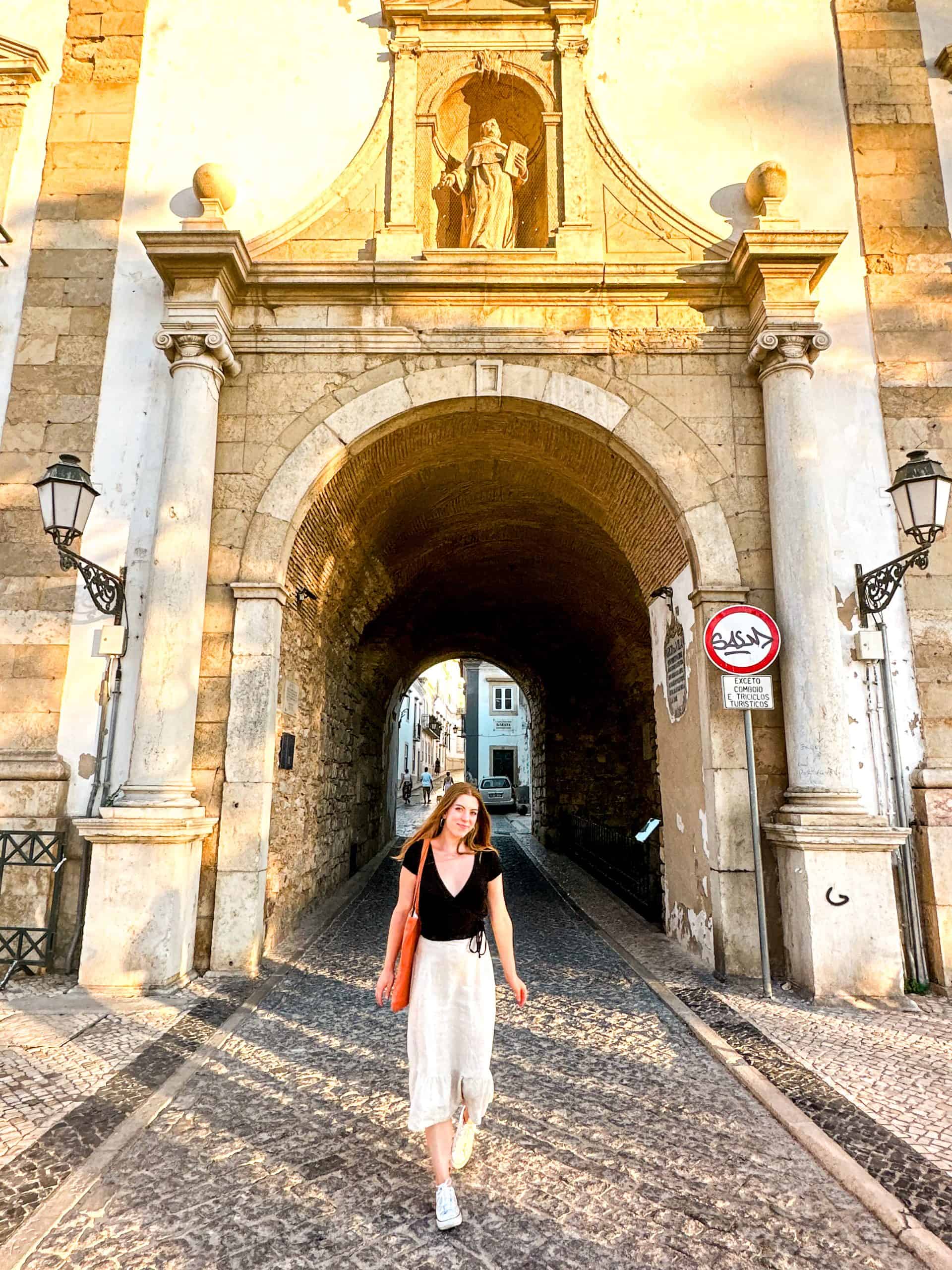 woman in front of the Arco da Vila arch in Old Town in Faro, Portugal