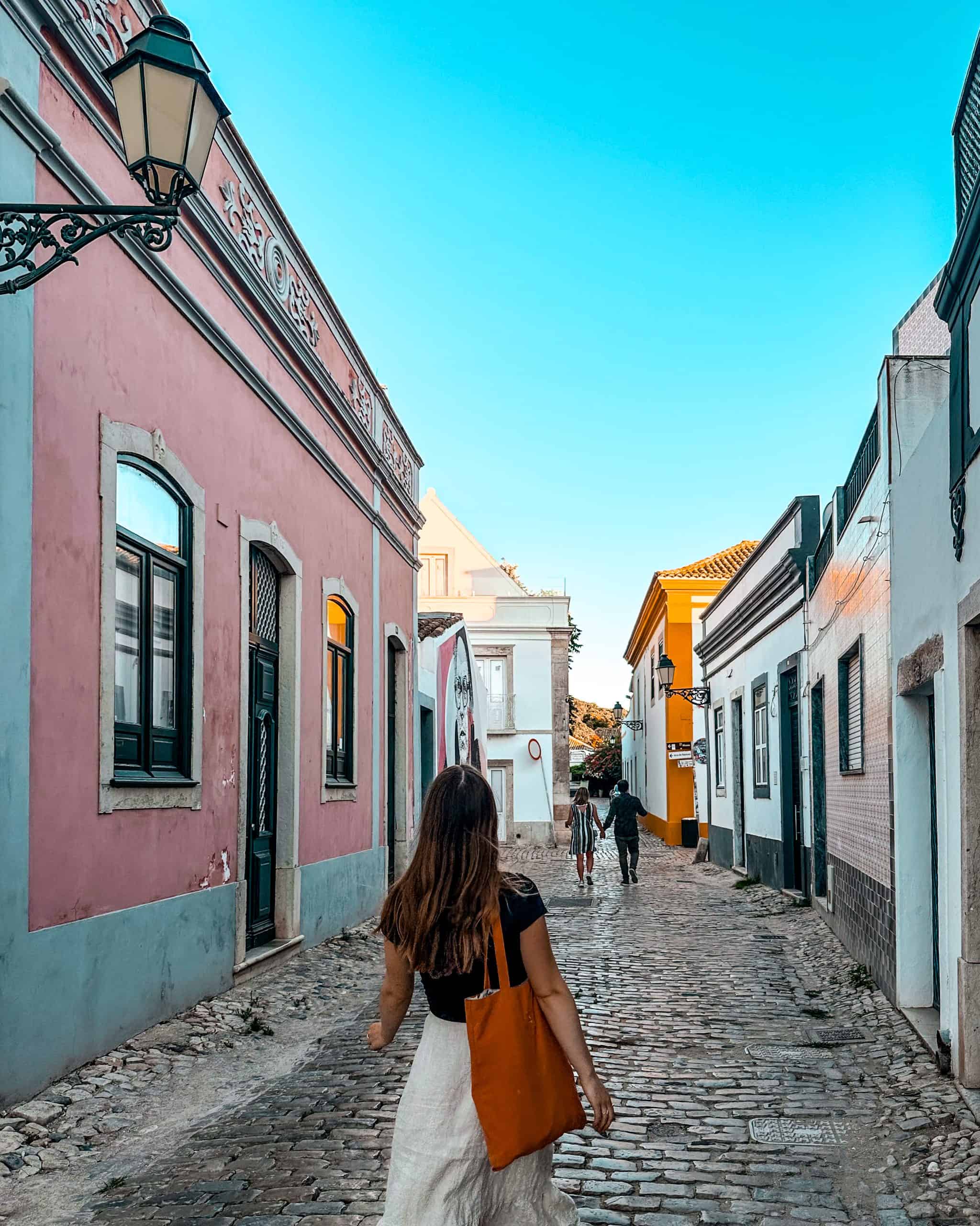 woman walking through the cobblestone streets in Faro, Portugal  surrounded by colorful buildings
