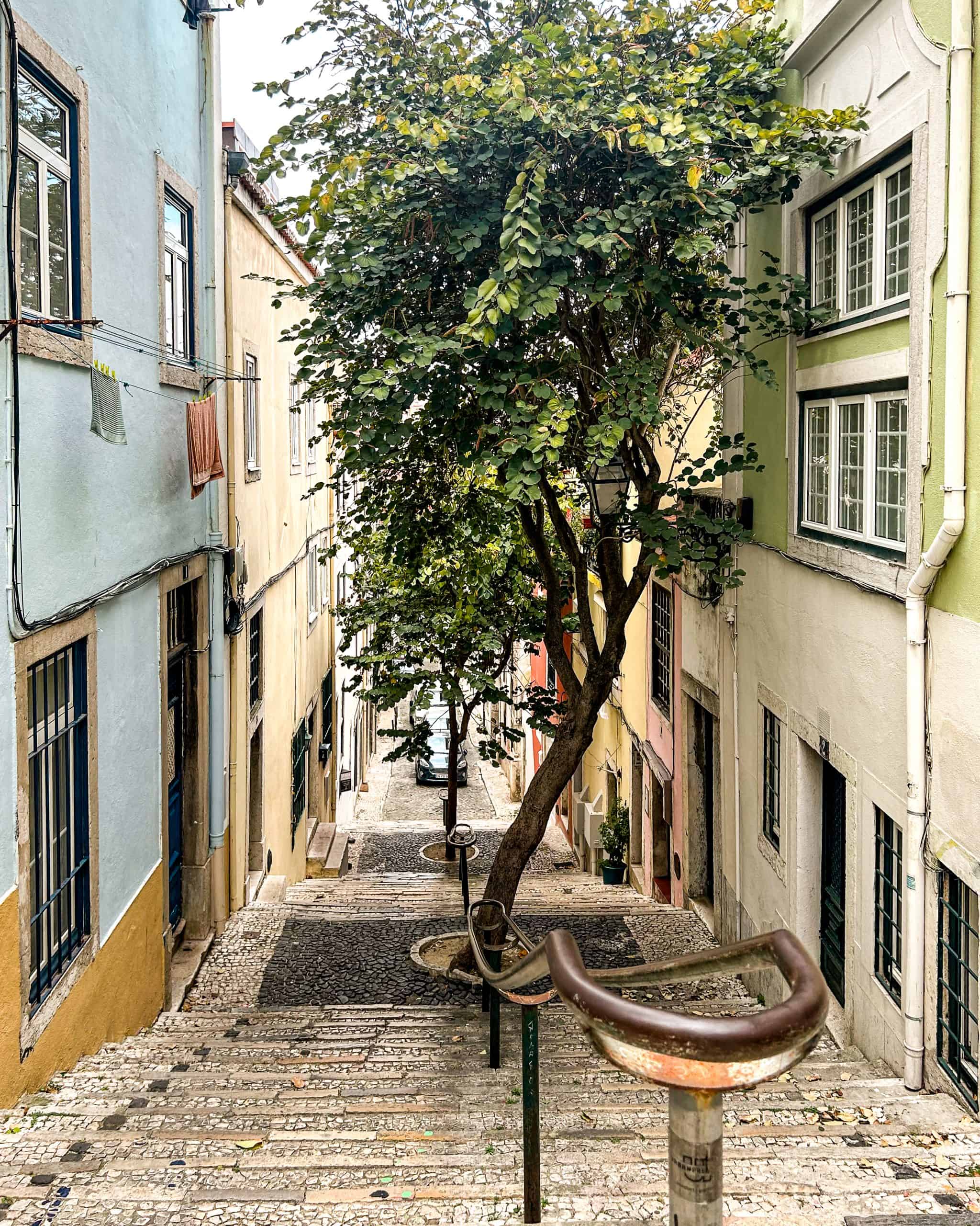 Narrow staircase lined with pastel buildings and greenery in a historic Lisbon, Portugal neighborhood