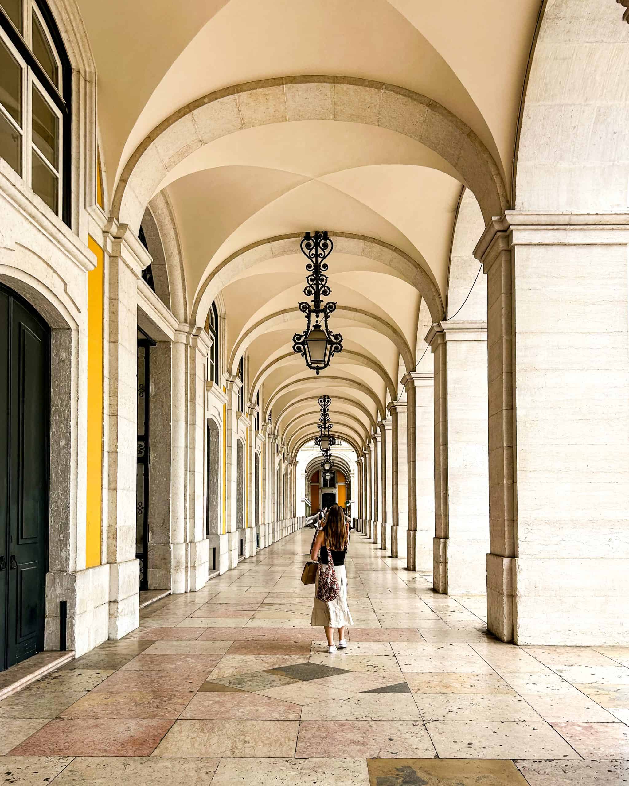 Arched walkway in Praça do Comércio with a woman walking through the iconic Lisbon, Portugal corridor