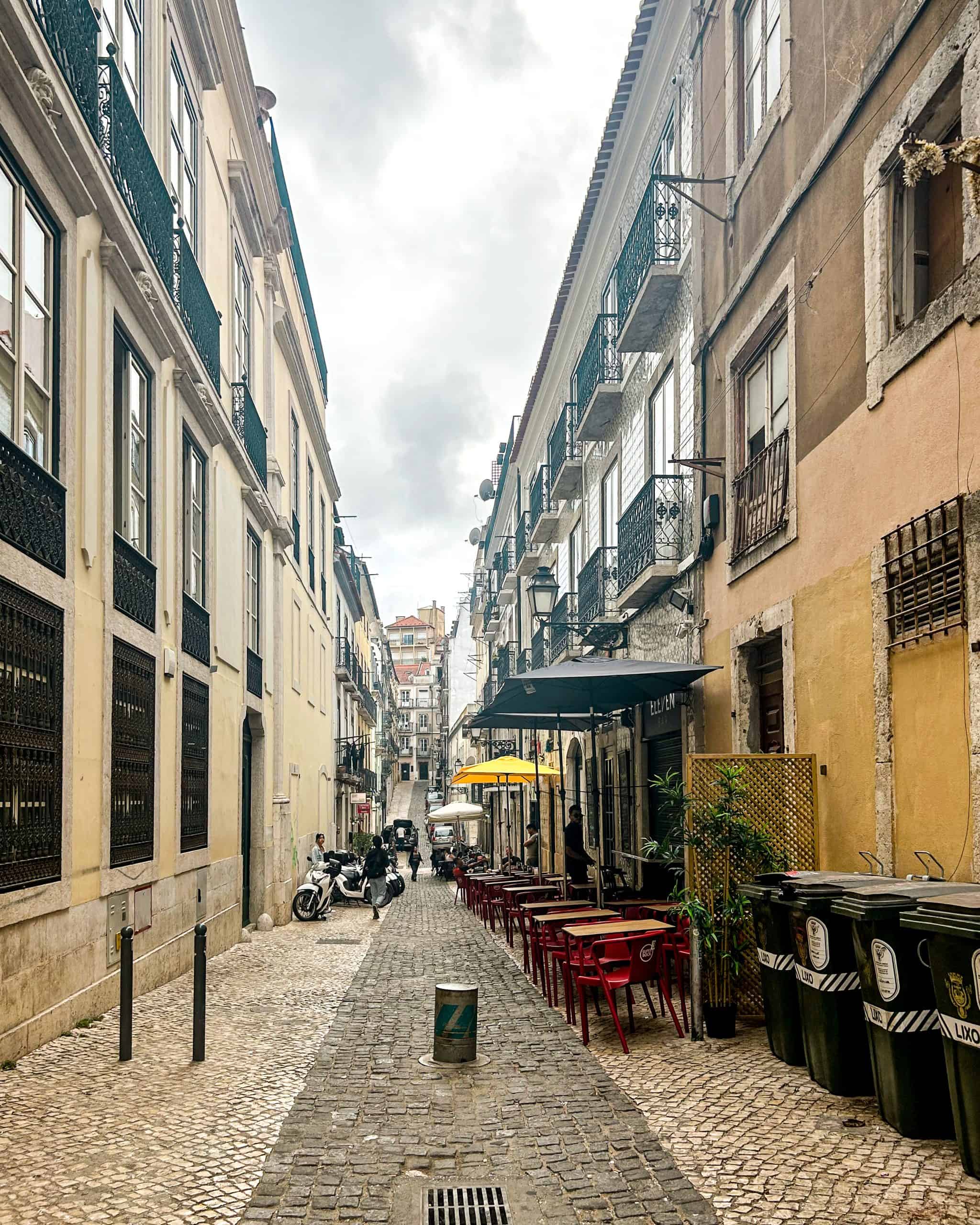 Cobblestone street with outdoor cafés and traditional architecture in central Lisbon, Portugal.