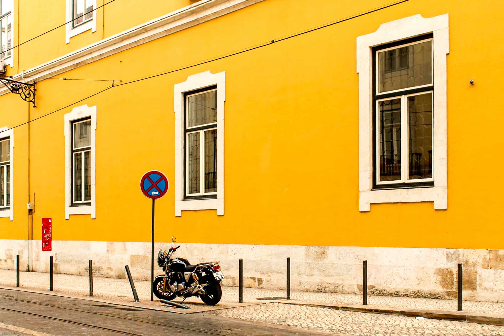 Motorcycle parked beside a bright yellow building on a quiet Lisbon, Portugal street