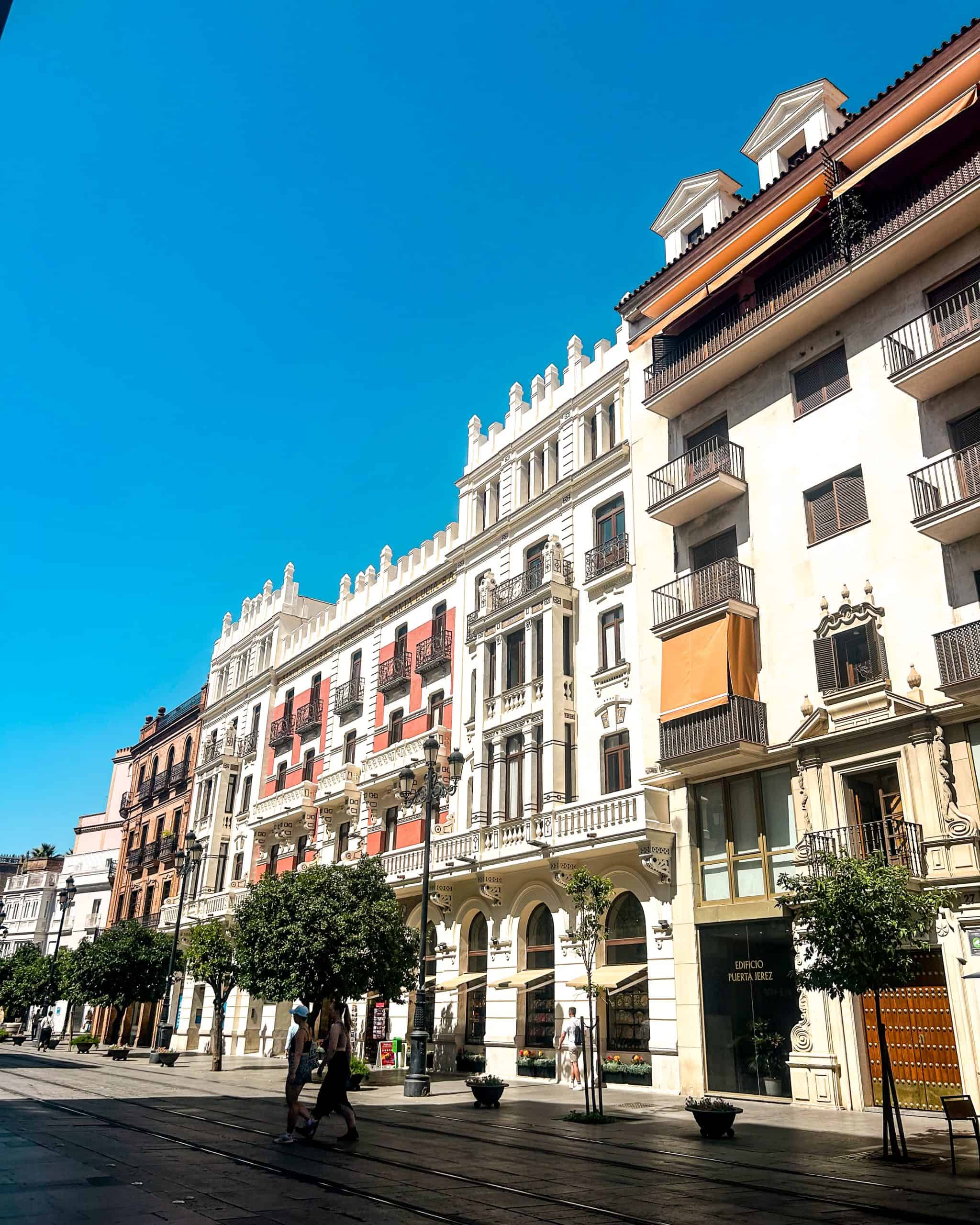 Historic street in the Arenal neighborhood of Seville, Spain, featuring traditional Andalusian architecture, colorful buildings, and a sunny pedestrian walkway.