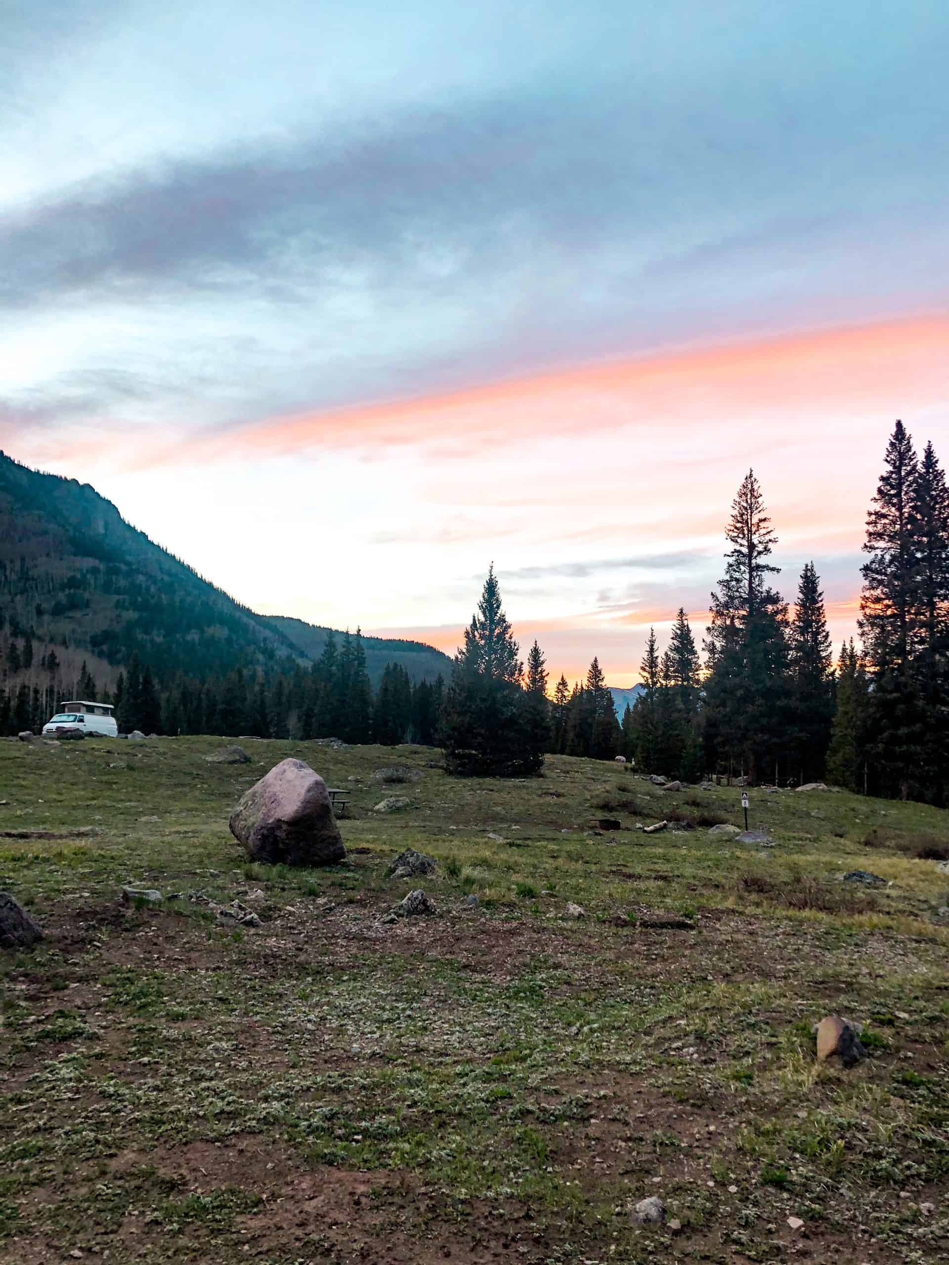 Sunset over alpine mountains and pine trees near Telluride, Colorado, with pastel skies and a peaceful mountain campsite
