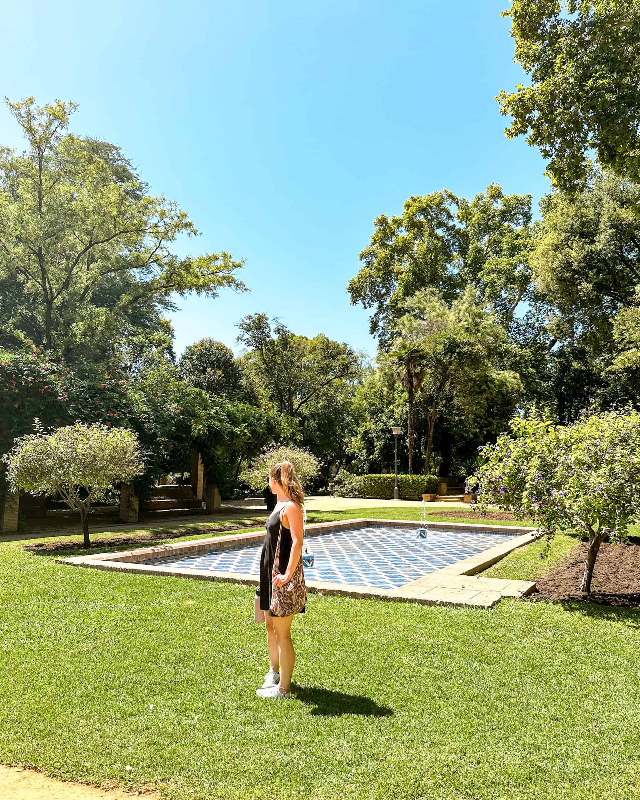 Traveler standing in the gardens of María Luisa Park in Seville, Spain, surrounded by lush greenery, tiled fountains, and peaceful Andalusian landscaping