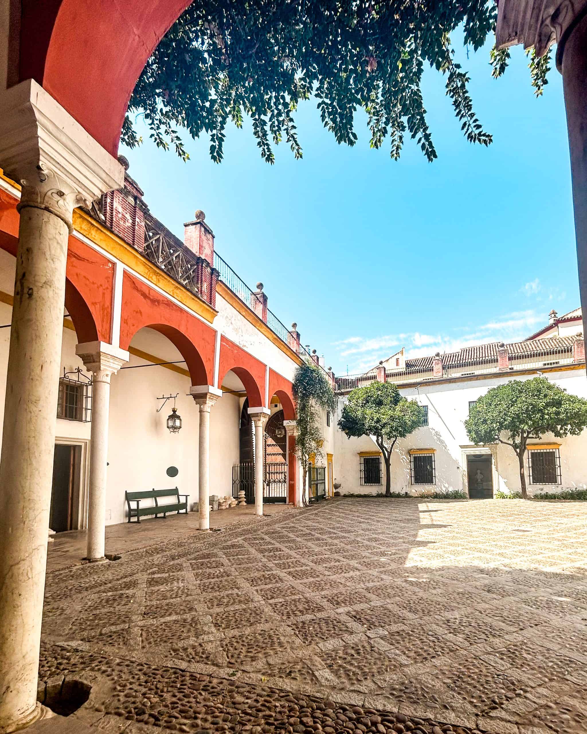 Traditional Andalusian courtyard in Seville, Spain, featuring arched walkways, cobblestone flooring, and vibrant red and yellow architecture.