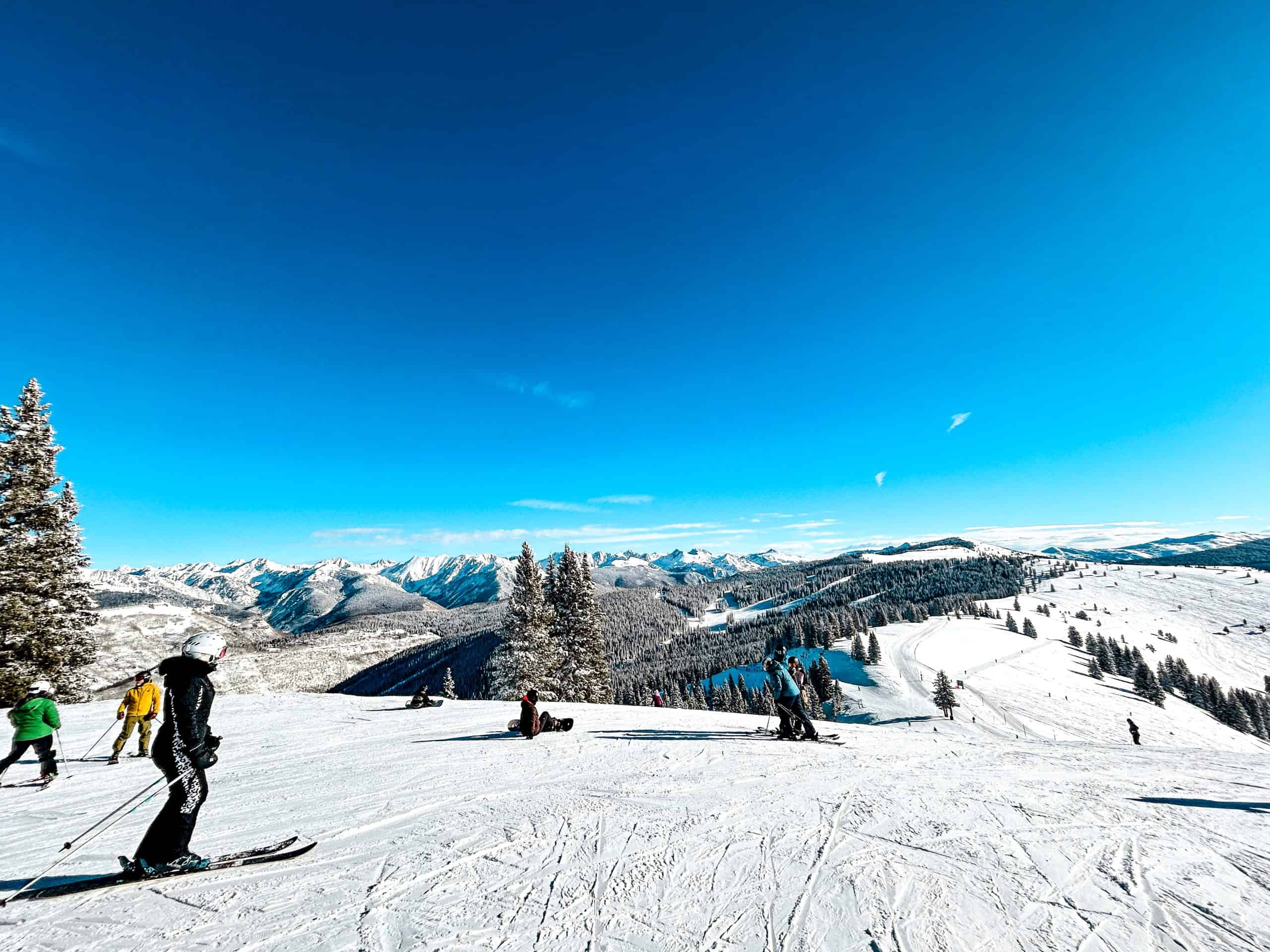 Skiers on a sunny winter day overlooking snow-covered mountains at Vail Ski Resort in Colorado.
