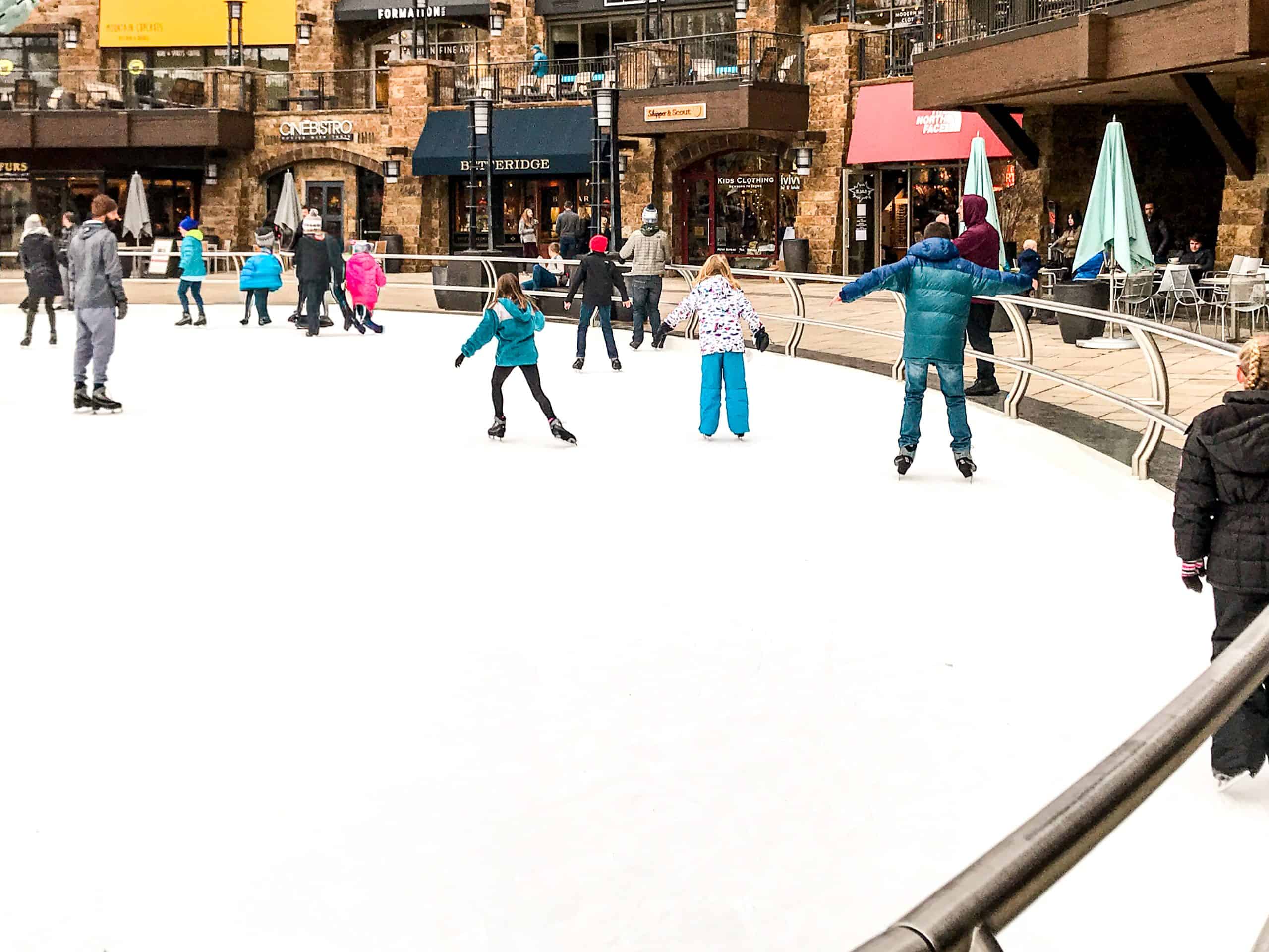 Ice skating rink in Vail Village surrounded by shops, restaurants, and families enjoying winter activities in Colorado.