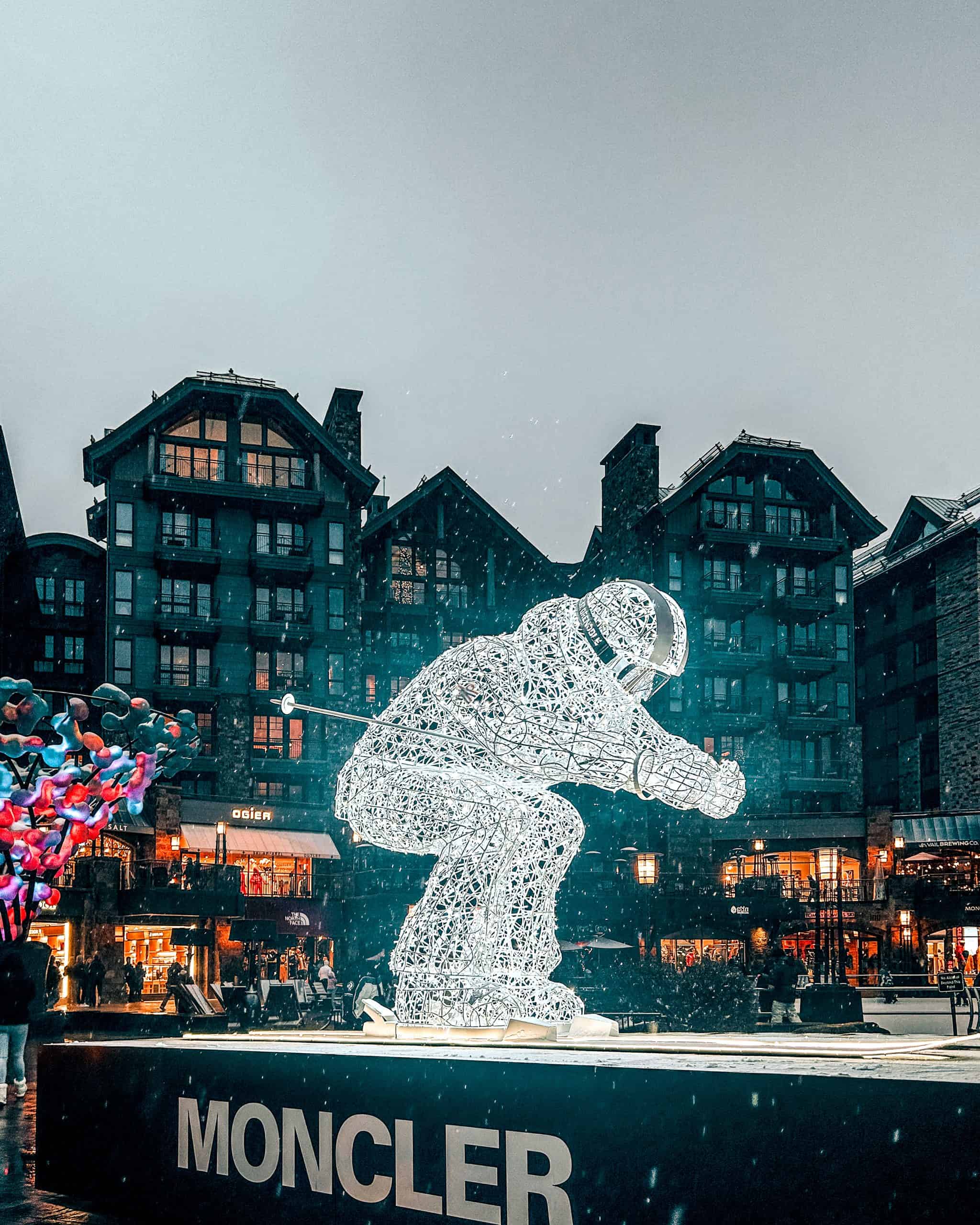 Illuminated skier sculpture in Vail Village at night with falling snow and luxury shops in Colorado