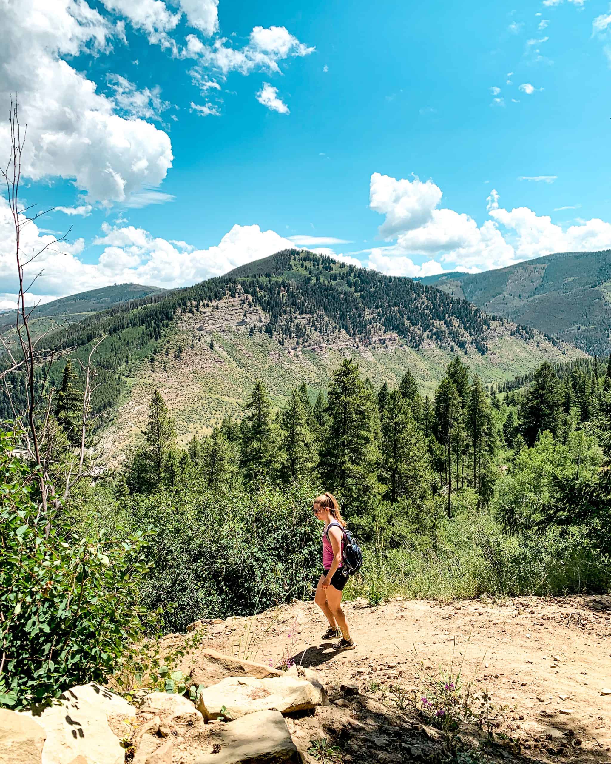 Hiker on a scenic mountain trail in Vail, Colorado with pine forests and alpine views on a summer hiking day