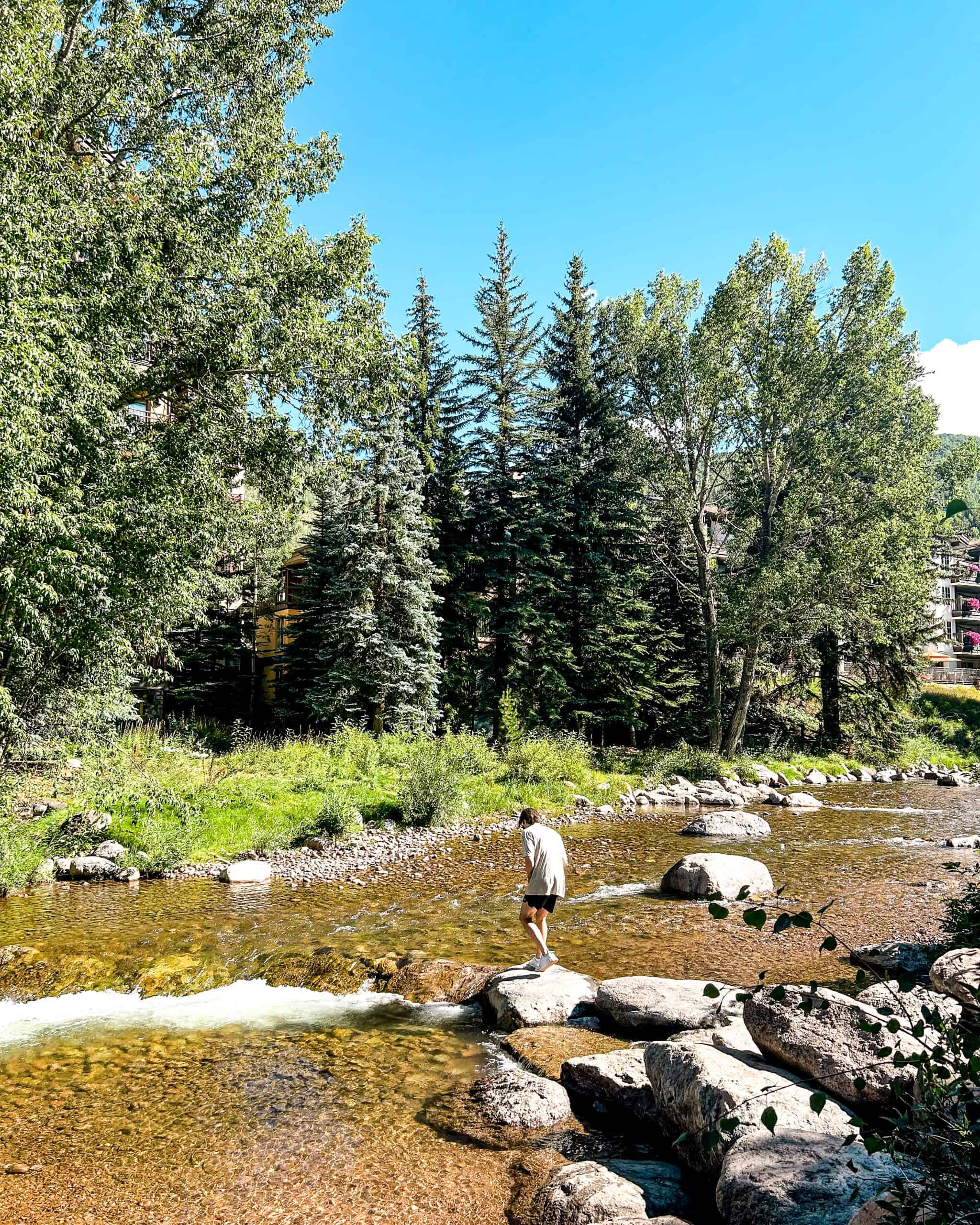 Walking across rocks in Gore Creek in Vail Village, Colorado surrounded by trees