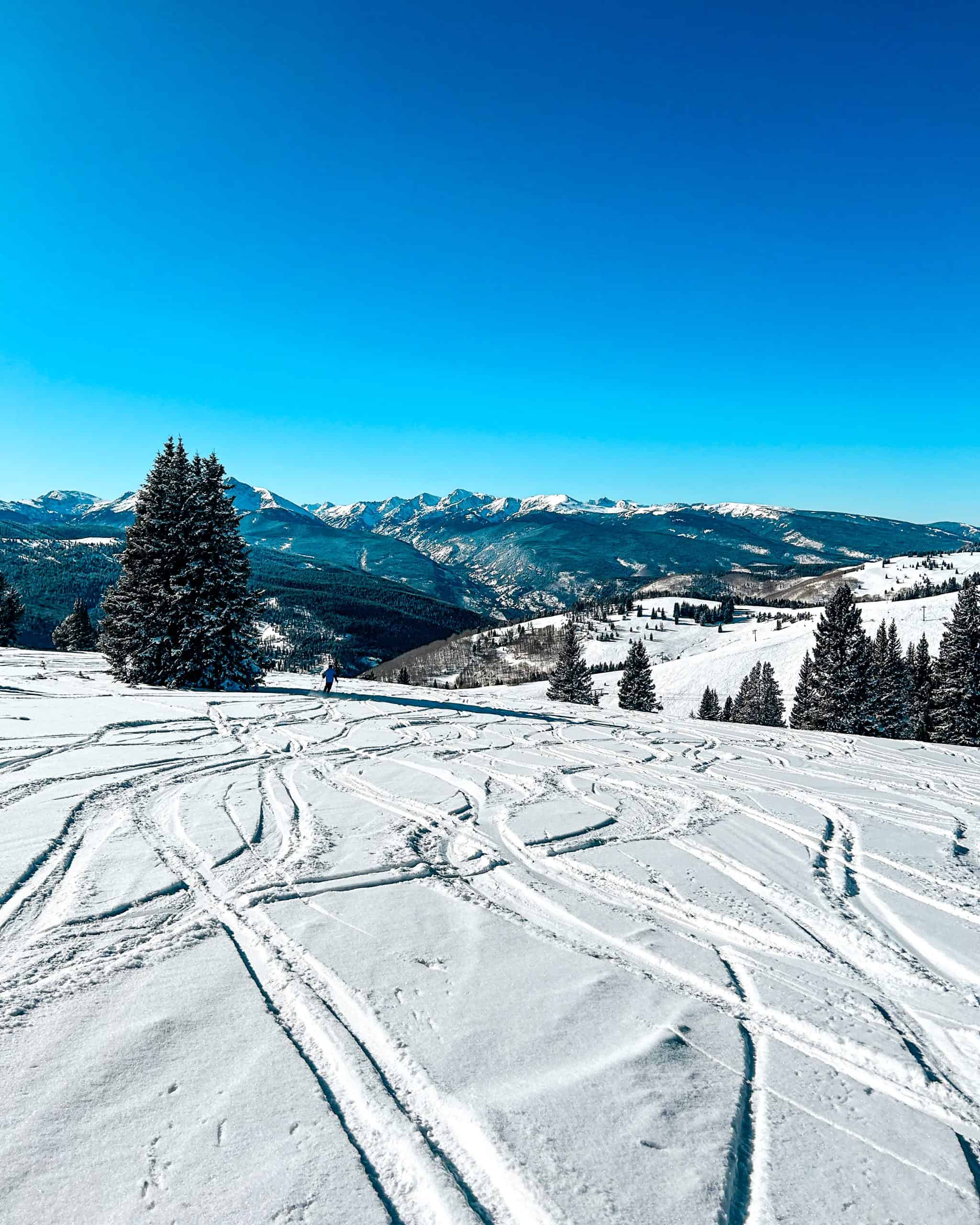 Ski runs with powder at a Colorado ski resort with expansive mountain scenery and bright blue sky