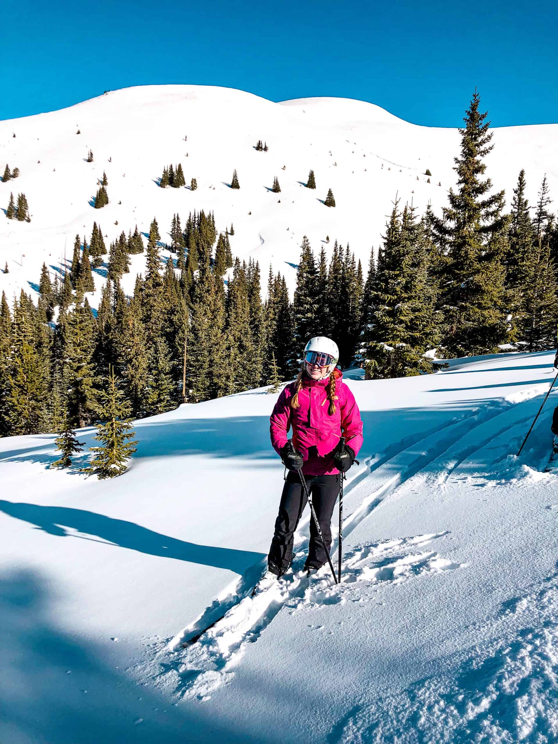 Skier standing on a powder-filled run at a Colorado ski resort surrounded by evergreen trees and alpine terrain