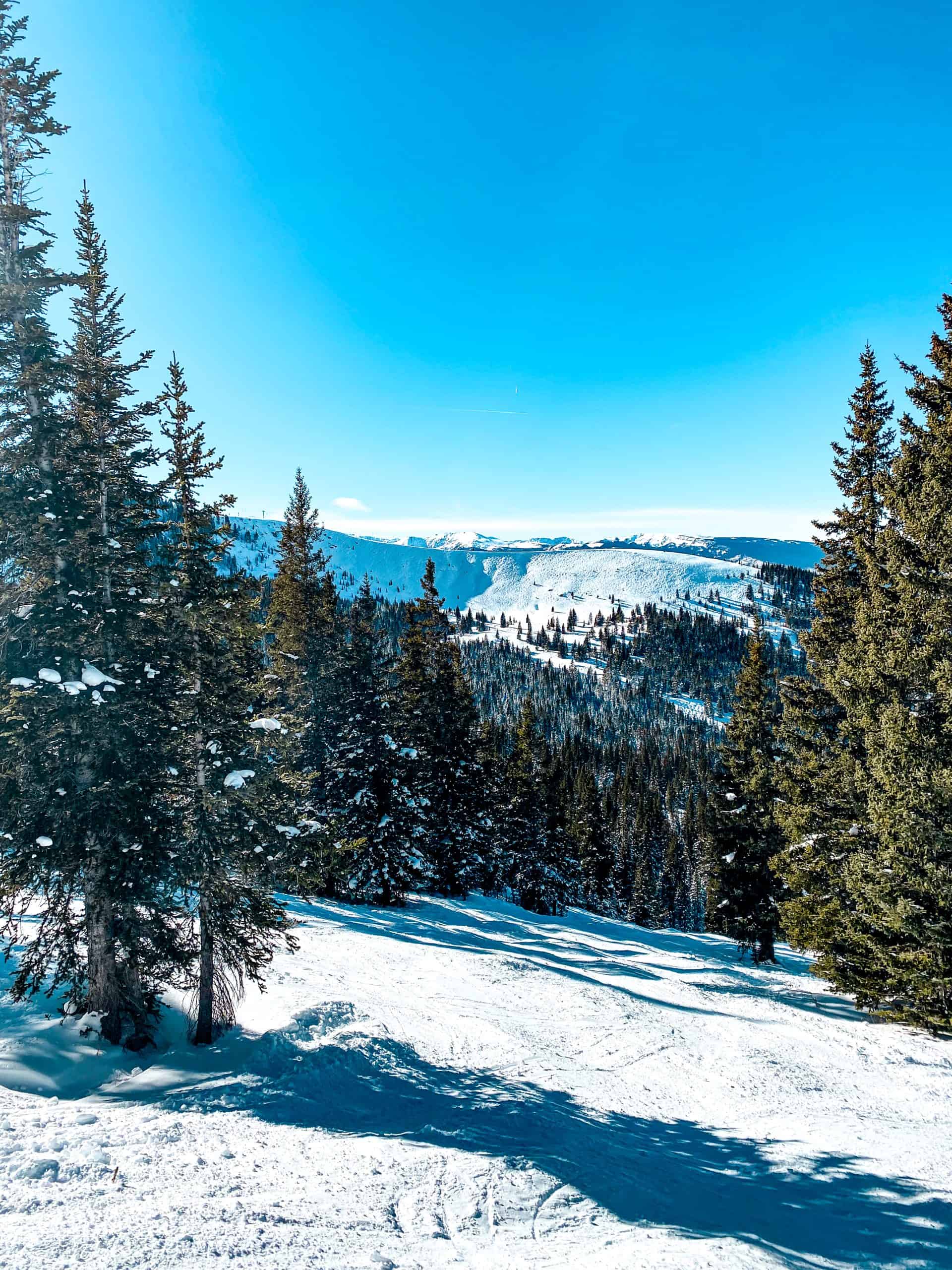 Scenic downhill ski run at a Colorado ski resort with forested mountains and open alpine bowls