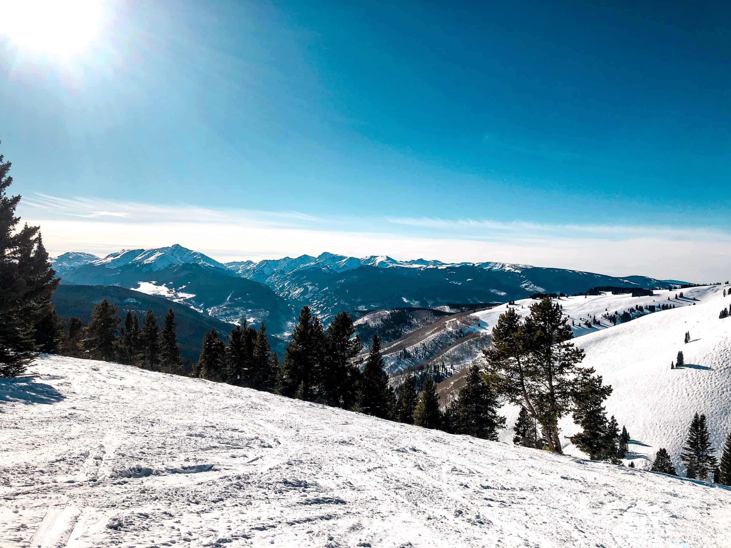 Peaceful snow-covered landscape at a Colorado ski resort with groomed trails, pine trees, and blue winter sky