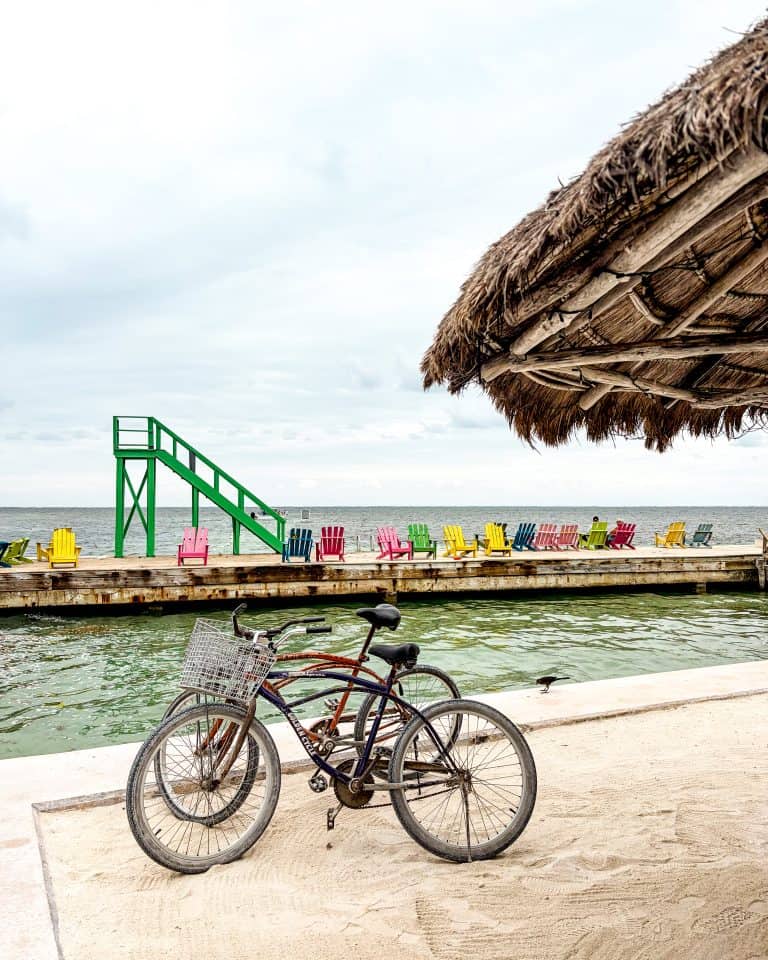 Bikes parked on sandy shore beside colorful chairs in Caye Caulker, Belize