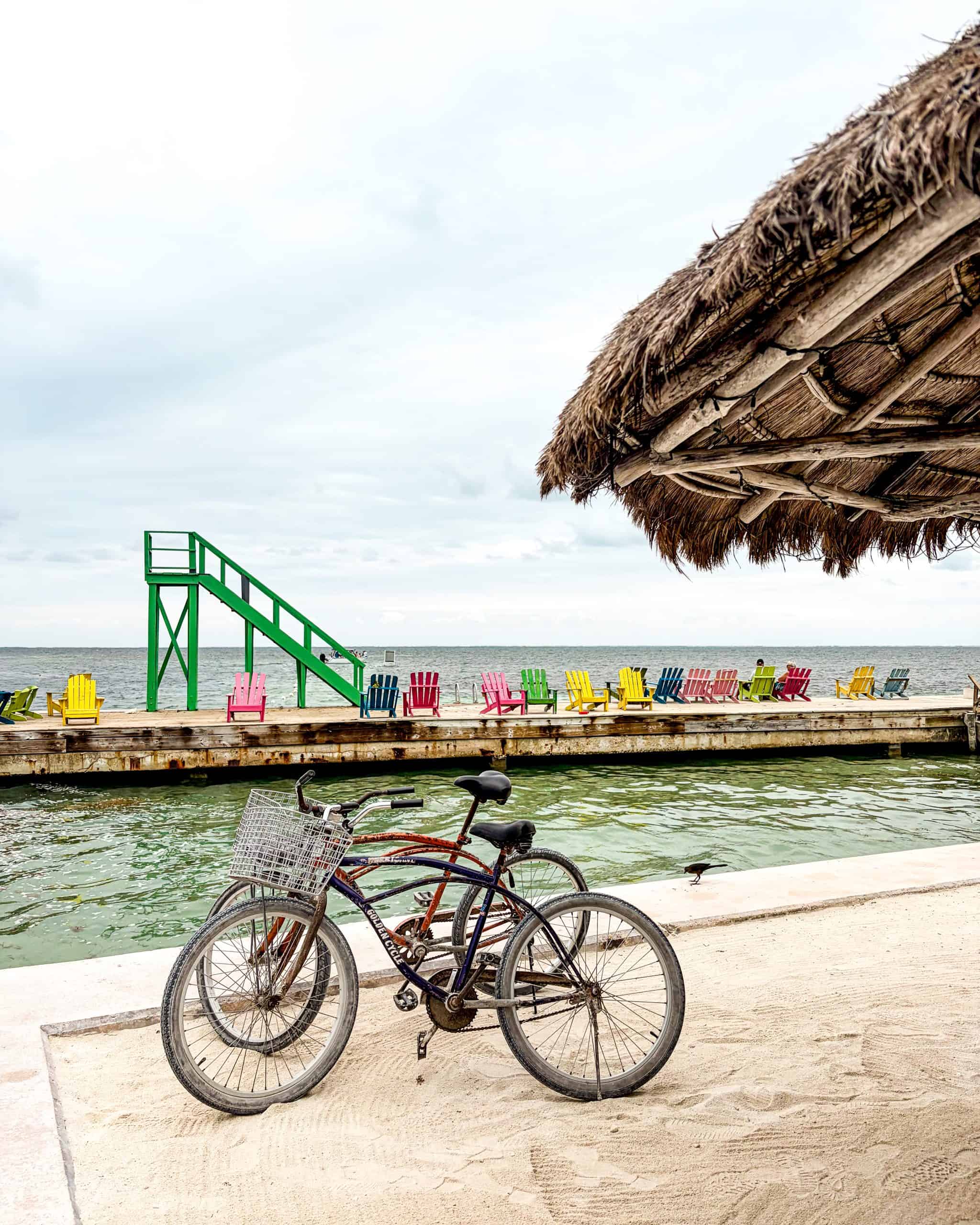 Bikes parked on sandy shore beside colorful chairs in Caye Caulker, Belize