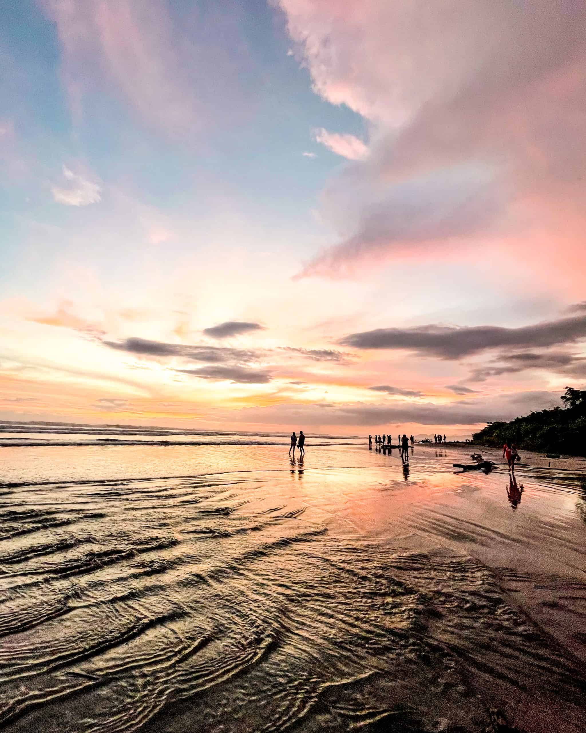 Wide sandy beach in Nosara, Costa Rica glowing under a vivid multicolored sunset sky