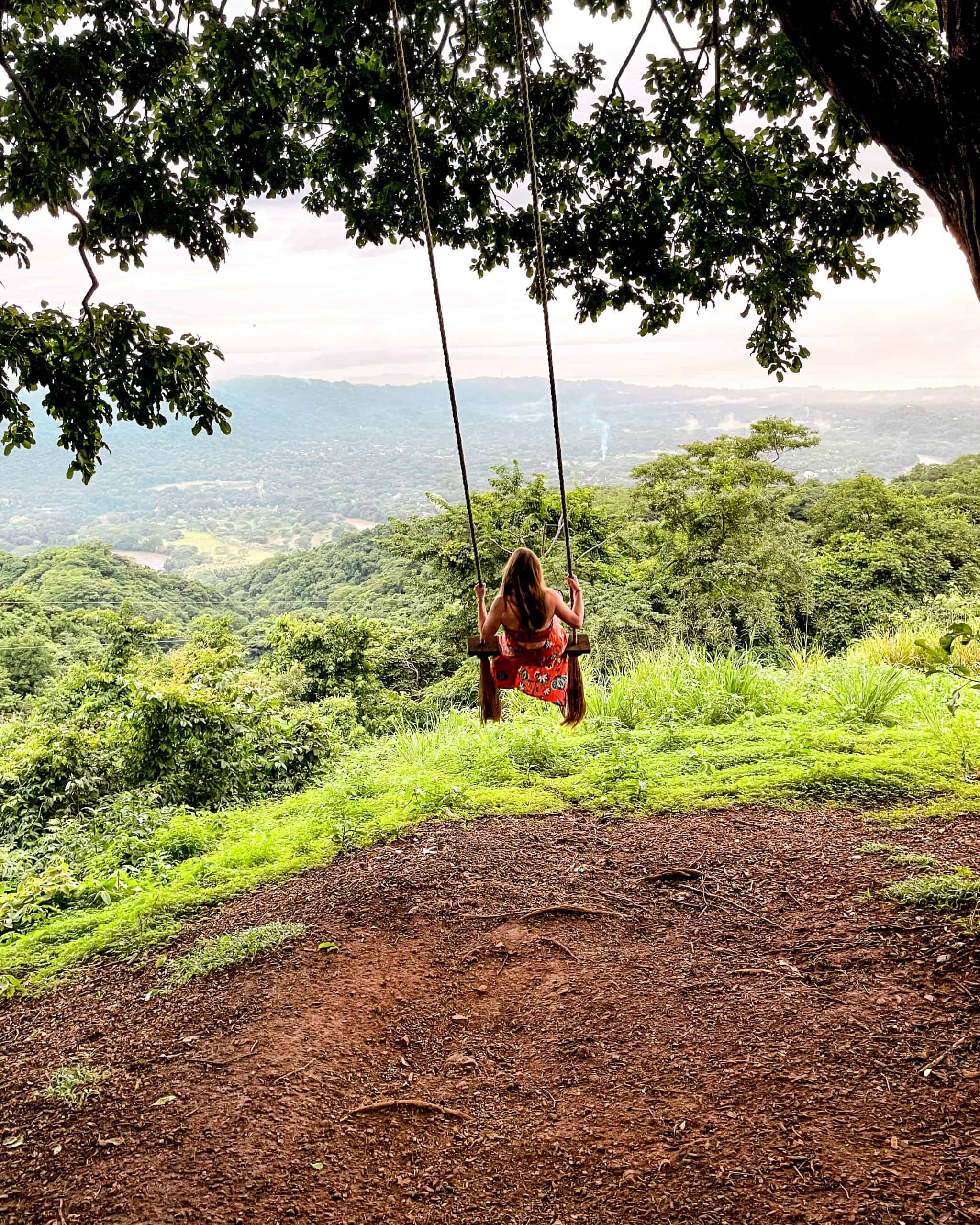Woman sitting on a swing in Nosara, Costa Rica, surrounded by lush green trees