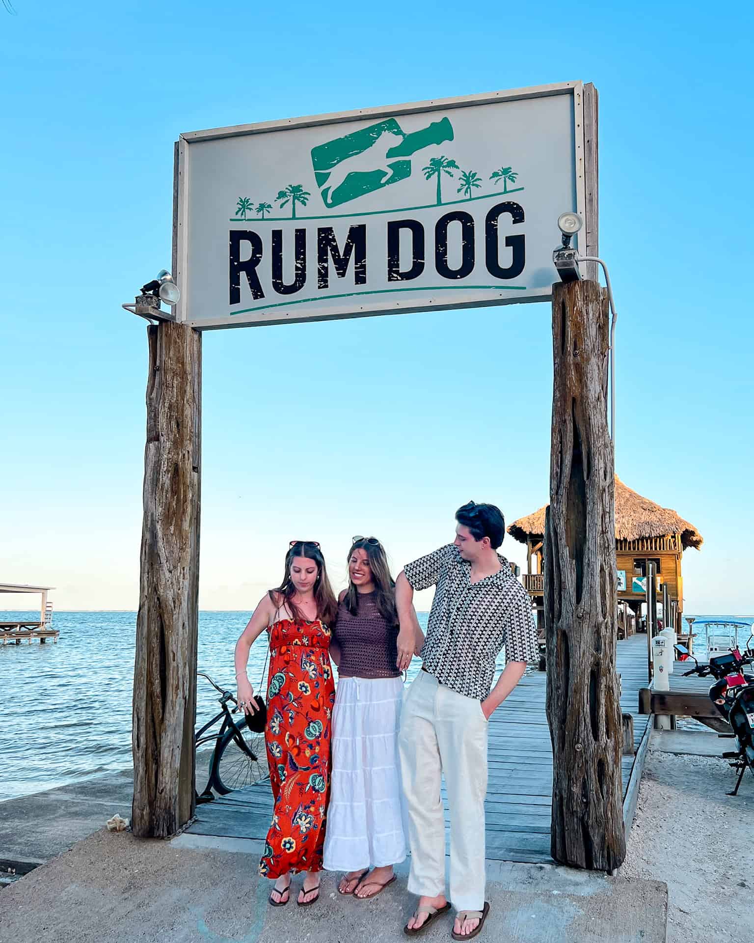 Three people standing on a dock beneath the Rum Dog sign in San Pedro, Belize