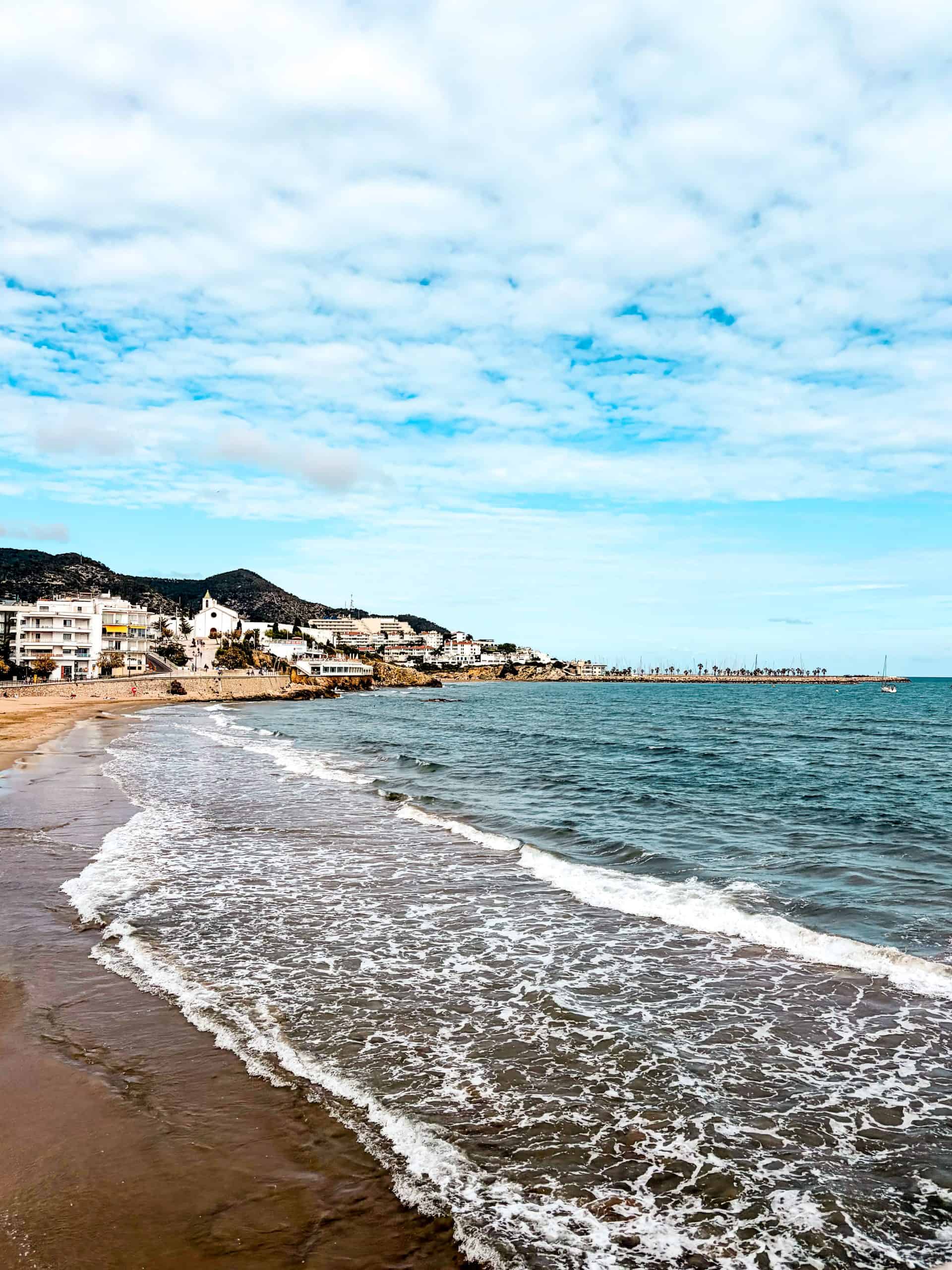 Sitges beach stretches along calm water with few visitors on a May morning