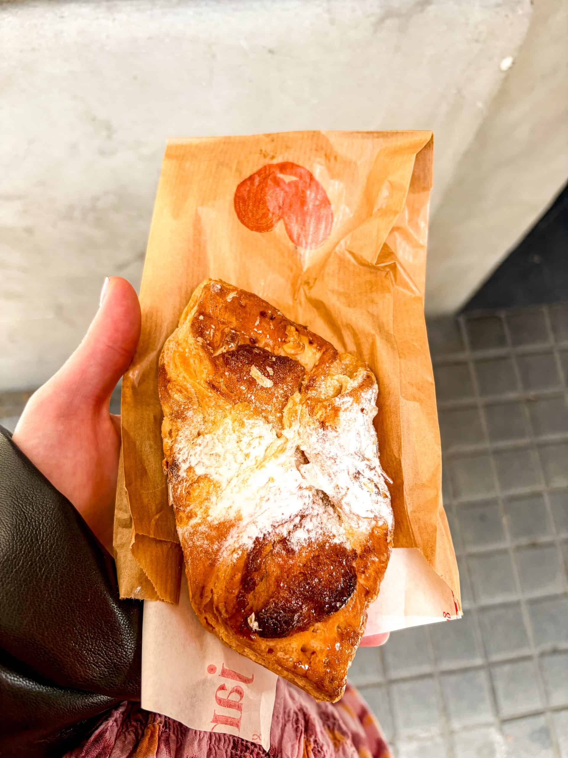 Hand holding a sugar-dusted gluten-free pastry on a paper bag from Jansana bakery