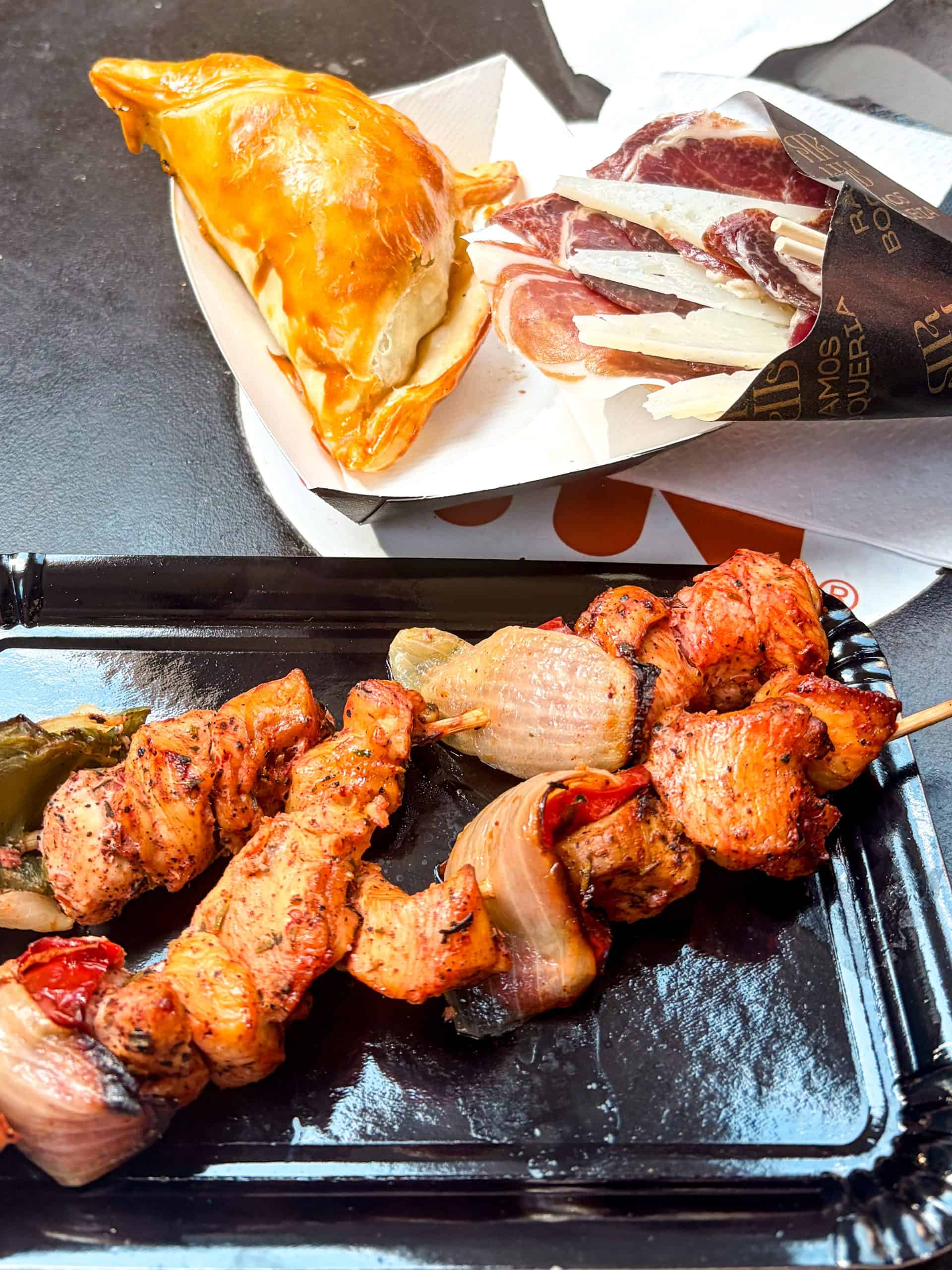 Cone of jamón ibérico and cheese beside an empanada and chicken skewers at La Boqueria