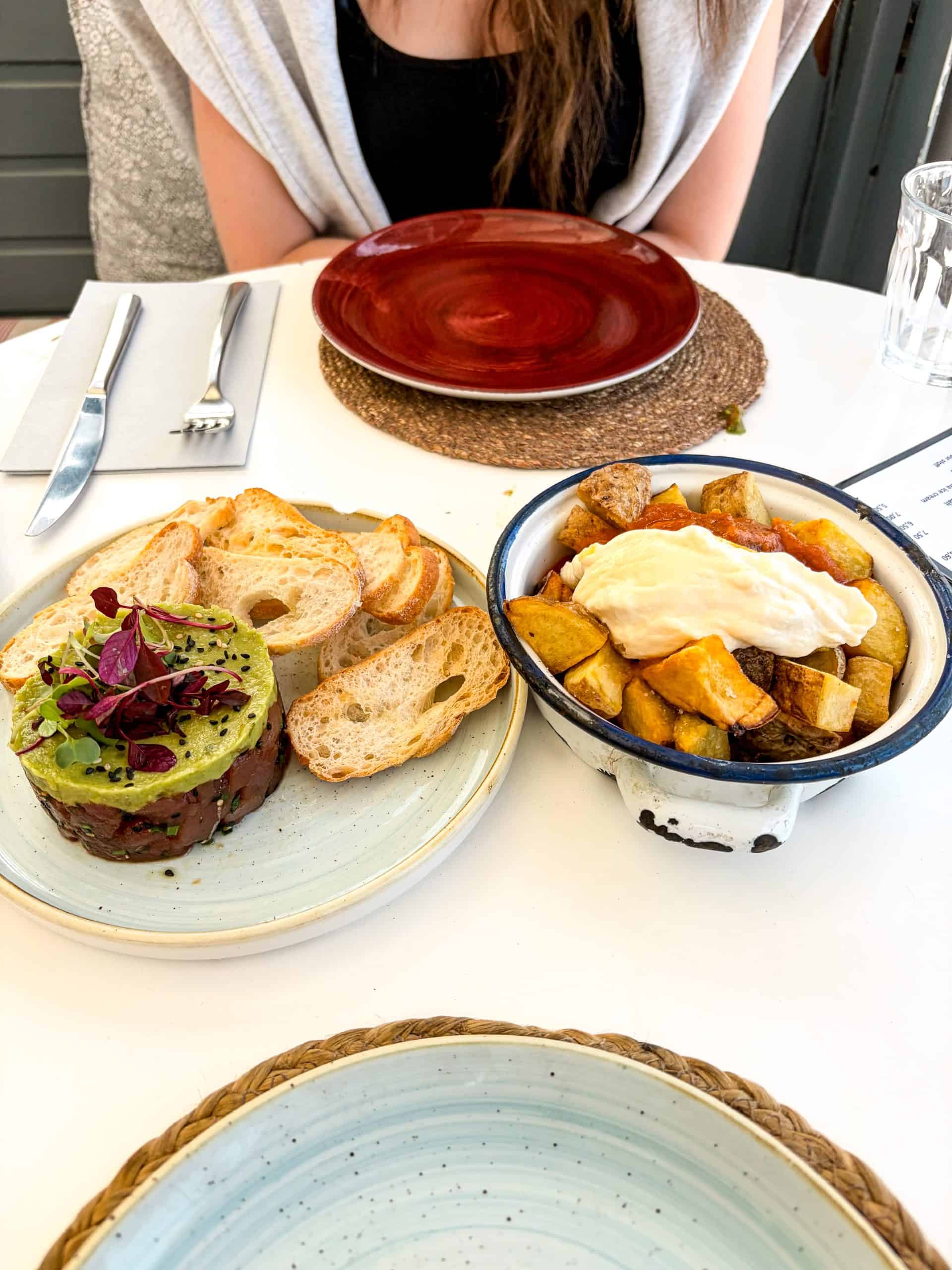 Patatas bravas topped with aioli beside avocado tuna tartare and toasted bread at Yamuna Sitges