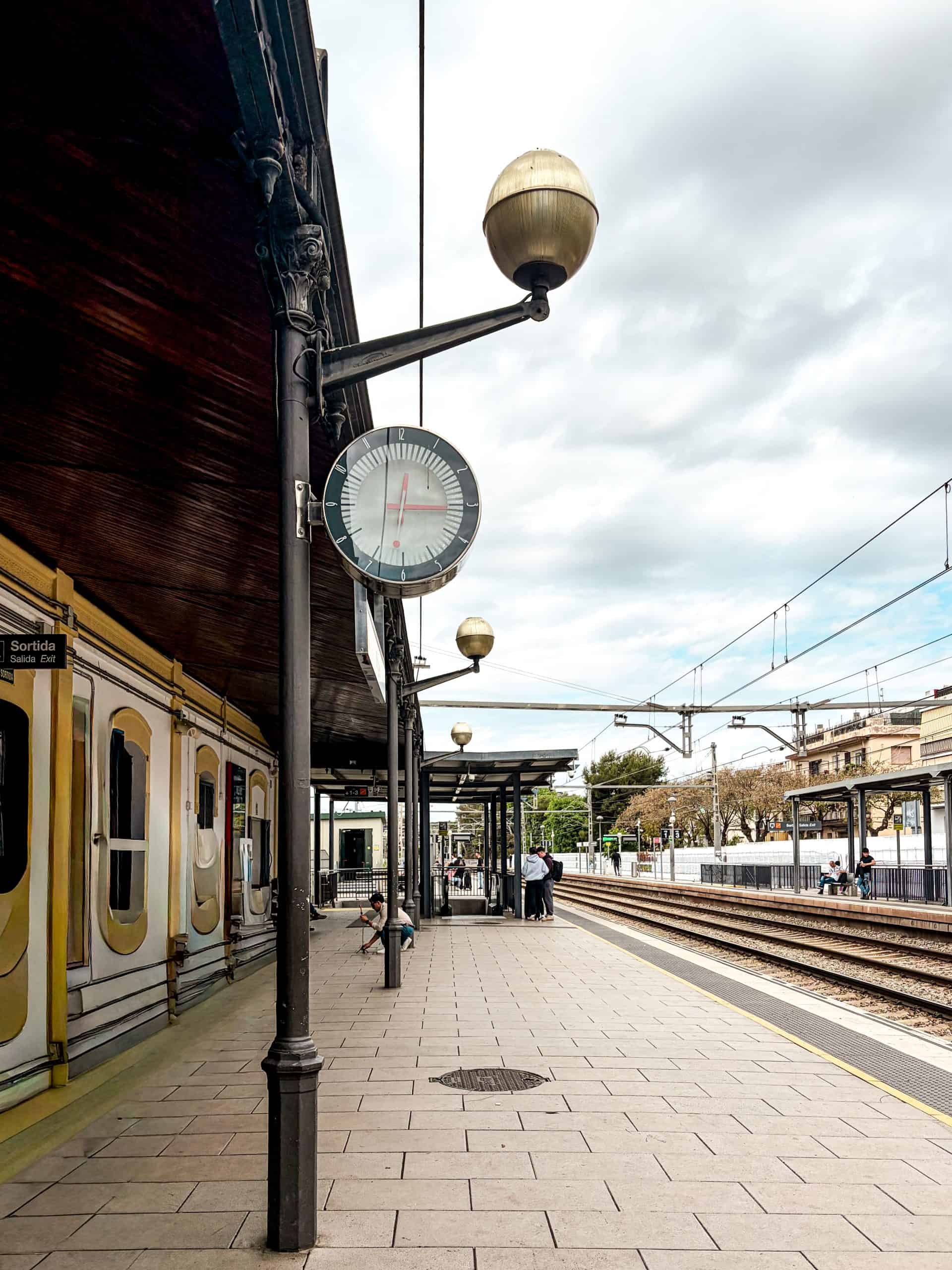 Sitges station platform with a vintage clock, globe lamps and empty tracks