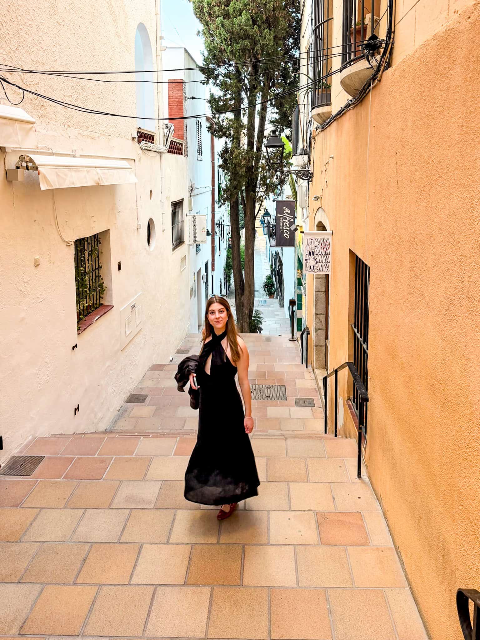 Woman climbing a tiled stairway street in Sitges below the Alfresco restaurant sign